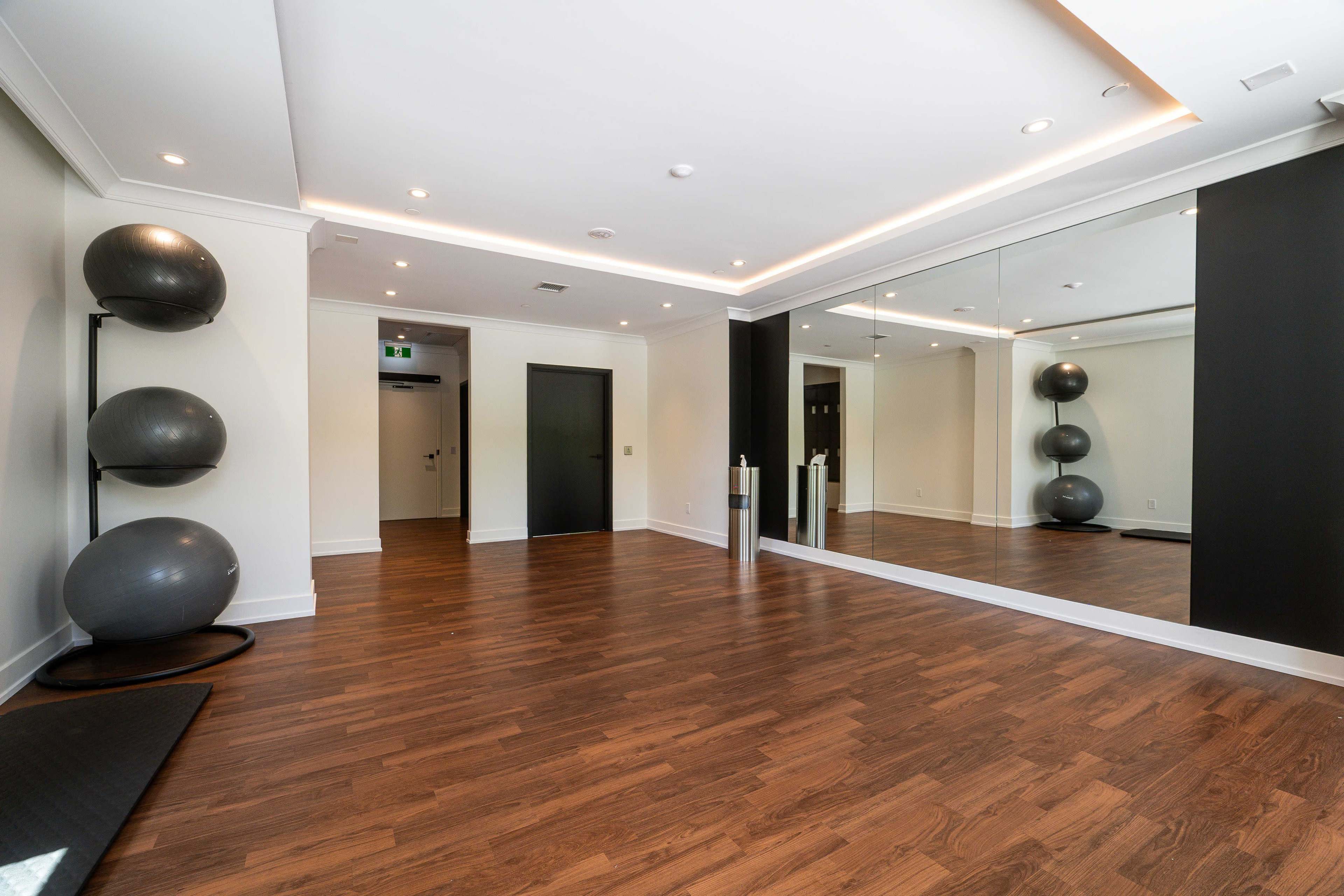 The image shows a spacious room with wooden floors, mirrored walls, and three black exercise balls stacked in a corner.