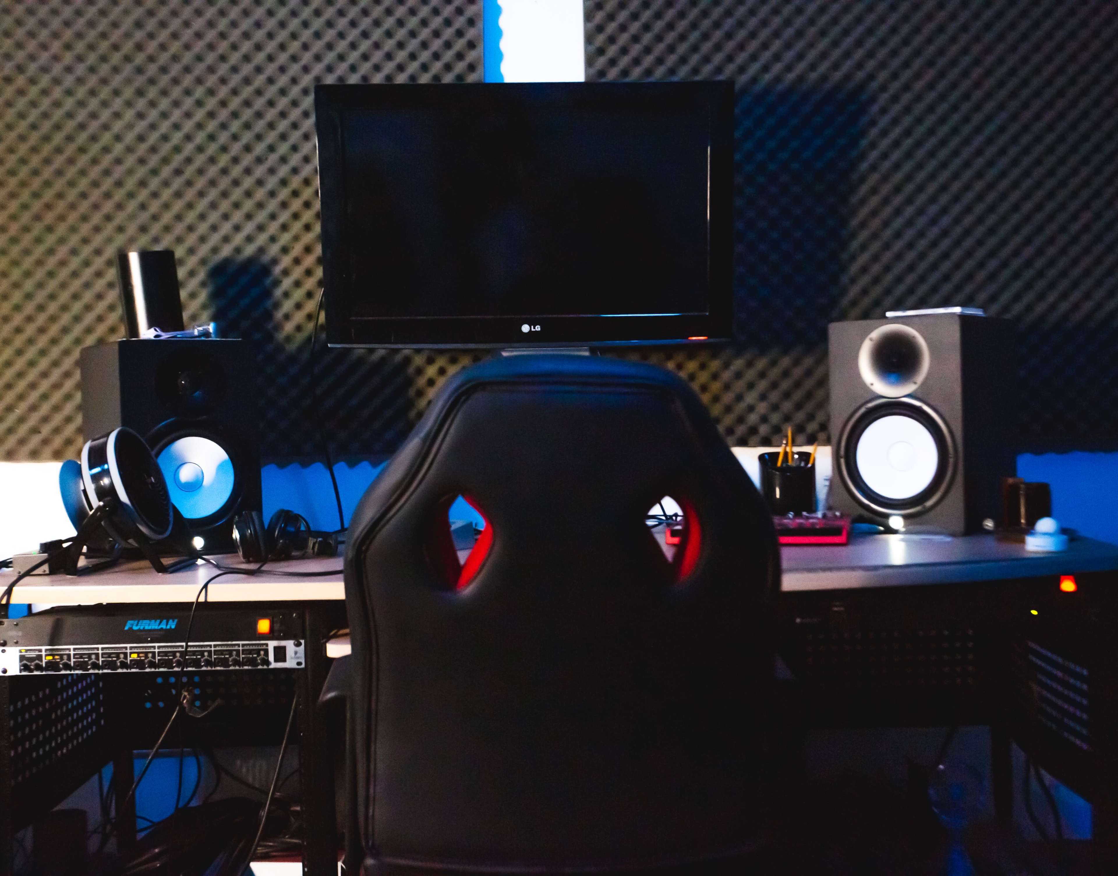 A music production studio with a desk, an office chair facing a television, and audio speakers on either side.