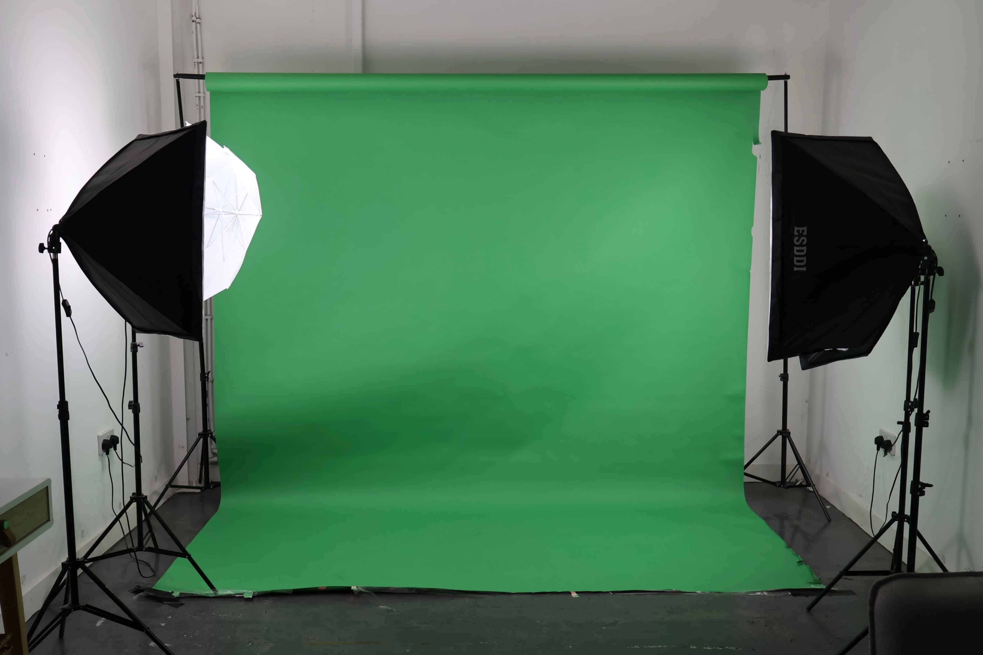 The image shows a photography studio setup with a green backdrop and two softbox lights positioned on either side.