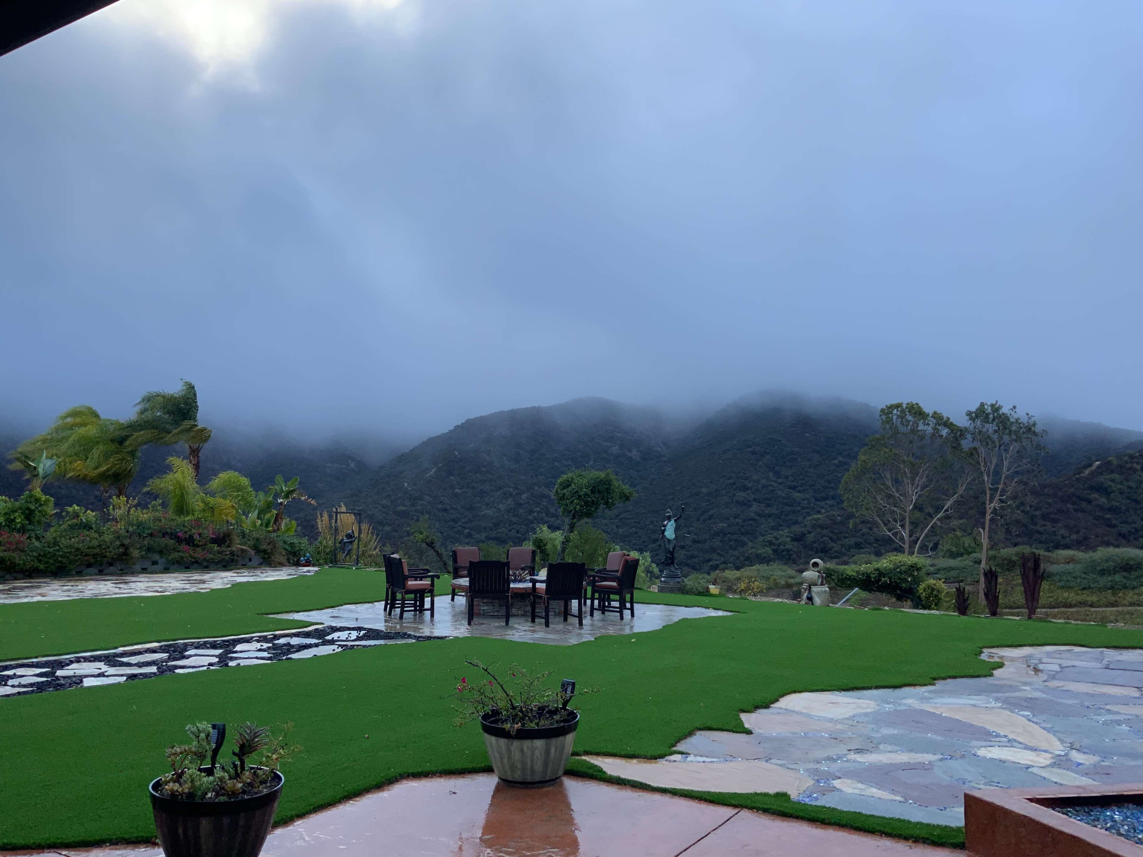 A patio area with a stone path and a set of six chairs around a table, overlooking a misty mountainous landscape.