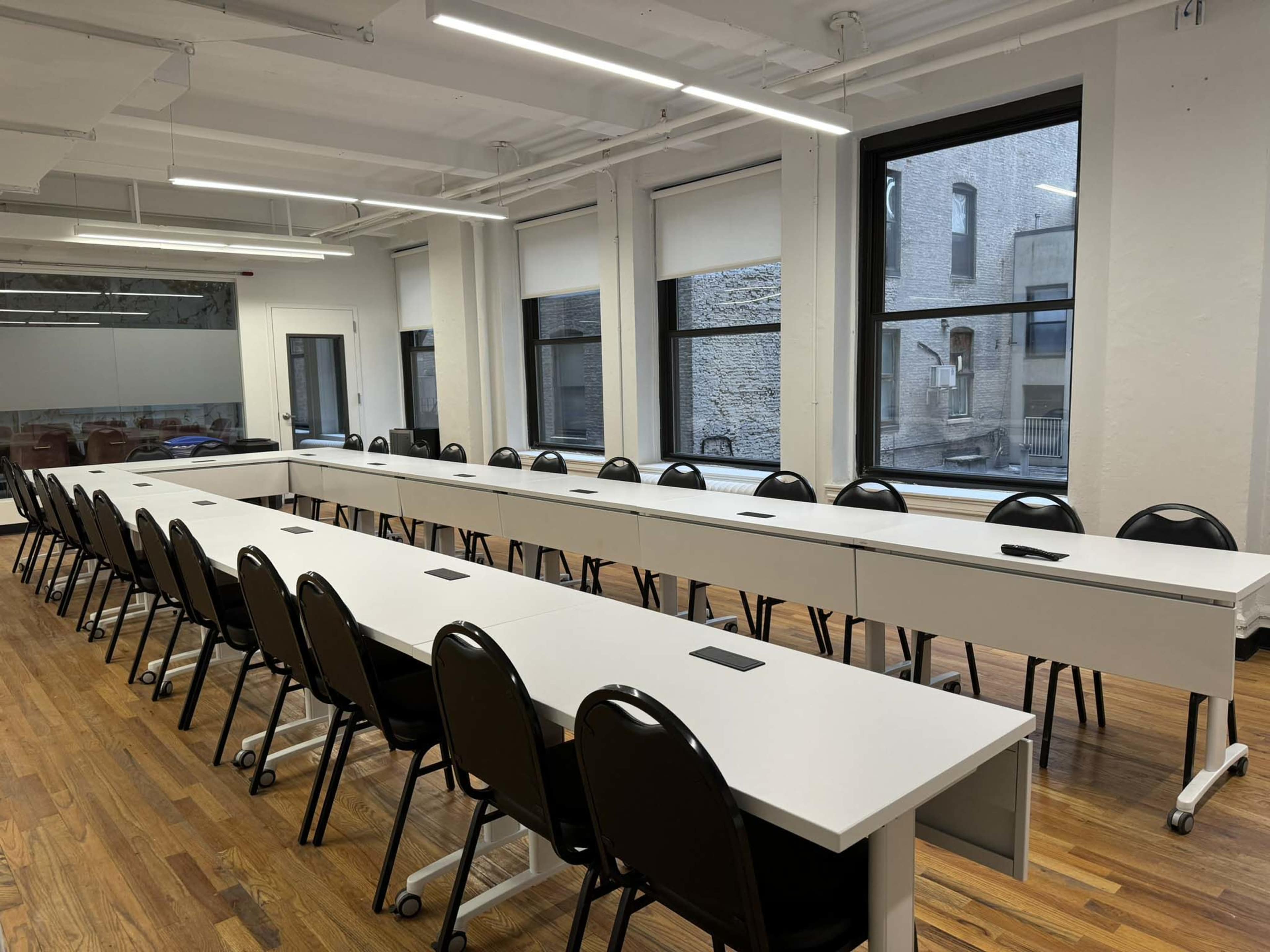 The image shows a spacious conference room with a long, white table surrounded by black chairs and large windows.