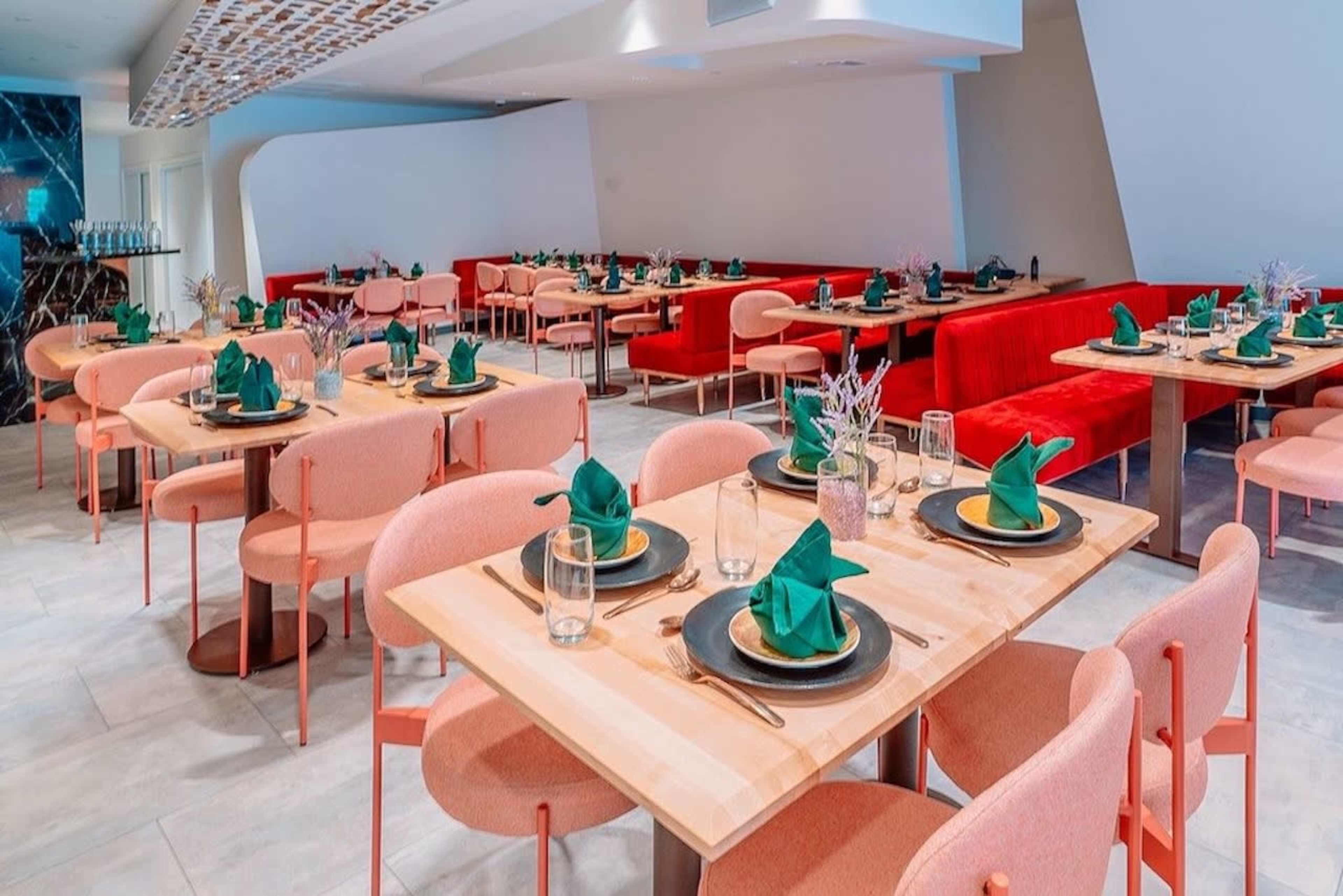 The image features a modern restaurant interior with multiple tables set with green napkins and tableware, surrounded by red seating.