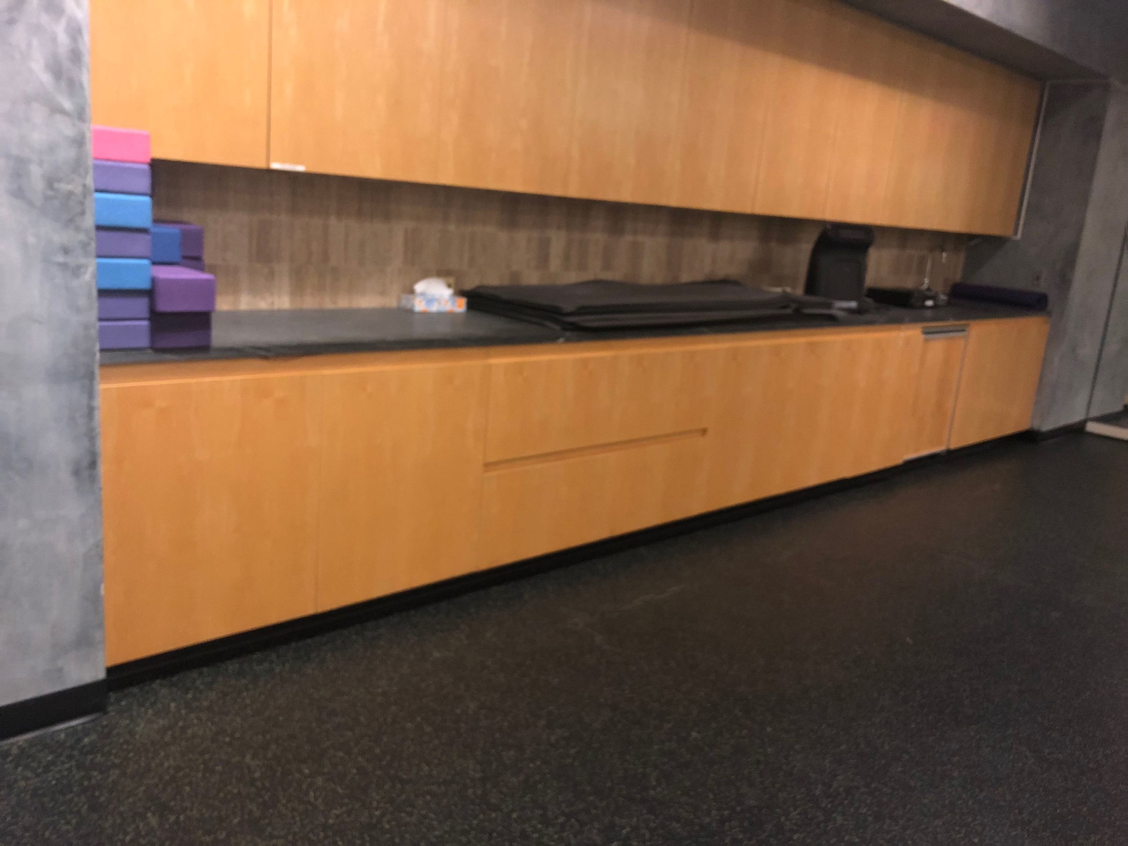 A wall-mounted wooden cabinetry above a black countertop in a room with a dark floor, alongside some purple and blue stacked items.