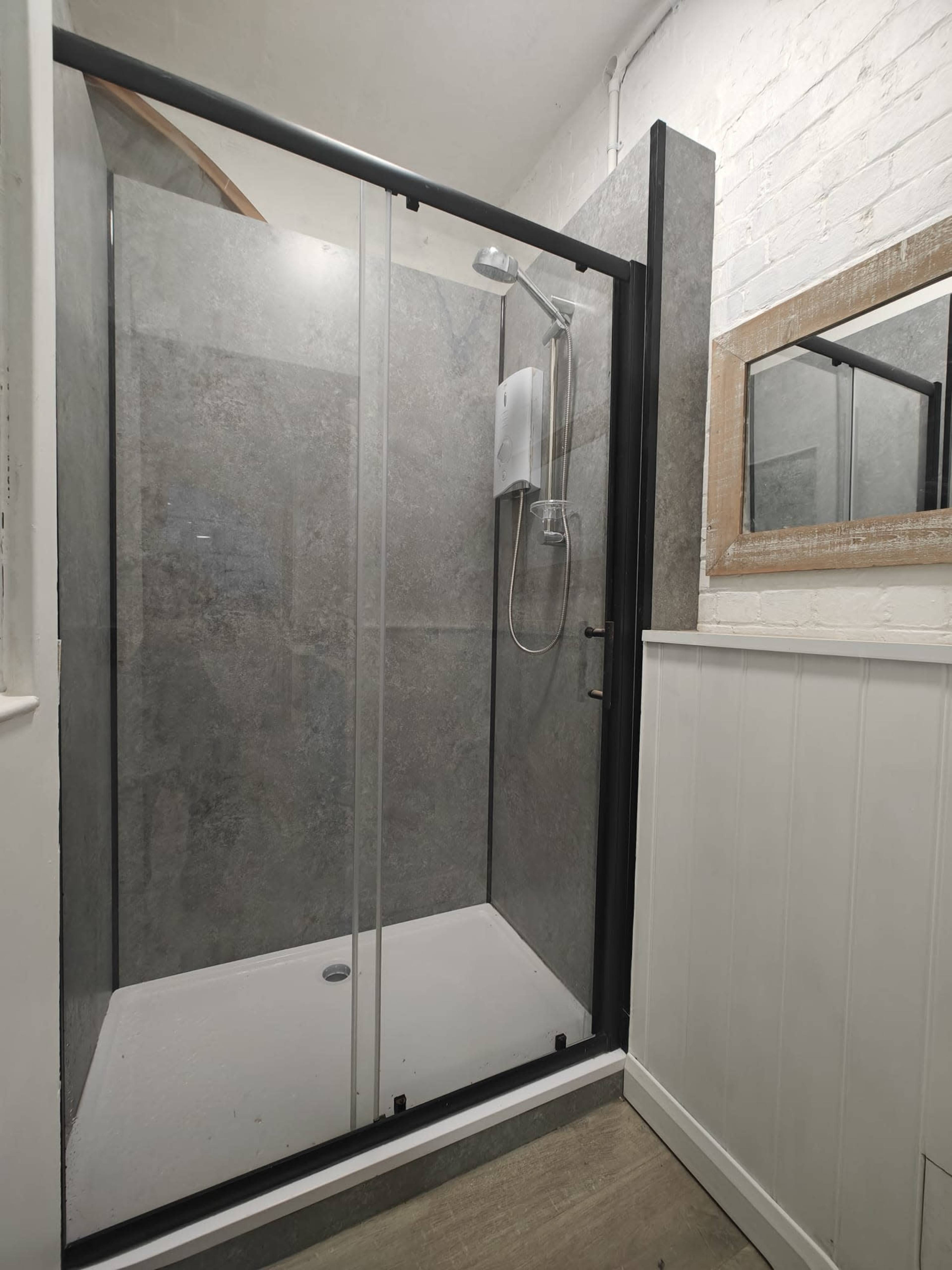 The image shows a modern shower enclosure with glass doors, featuring a rainfall showerhead and a white tiled floor in a bathroom.