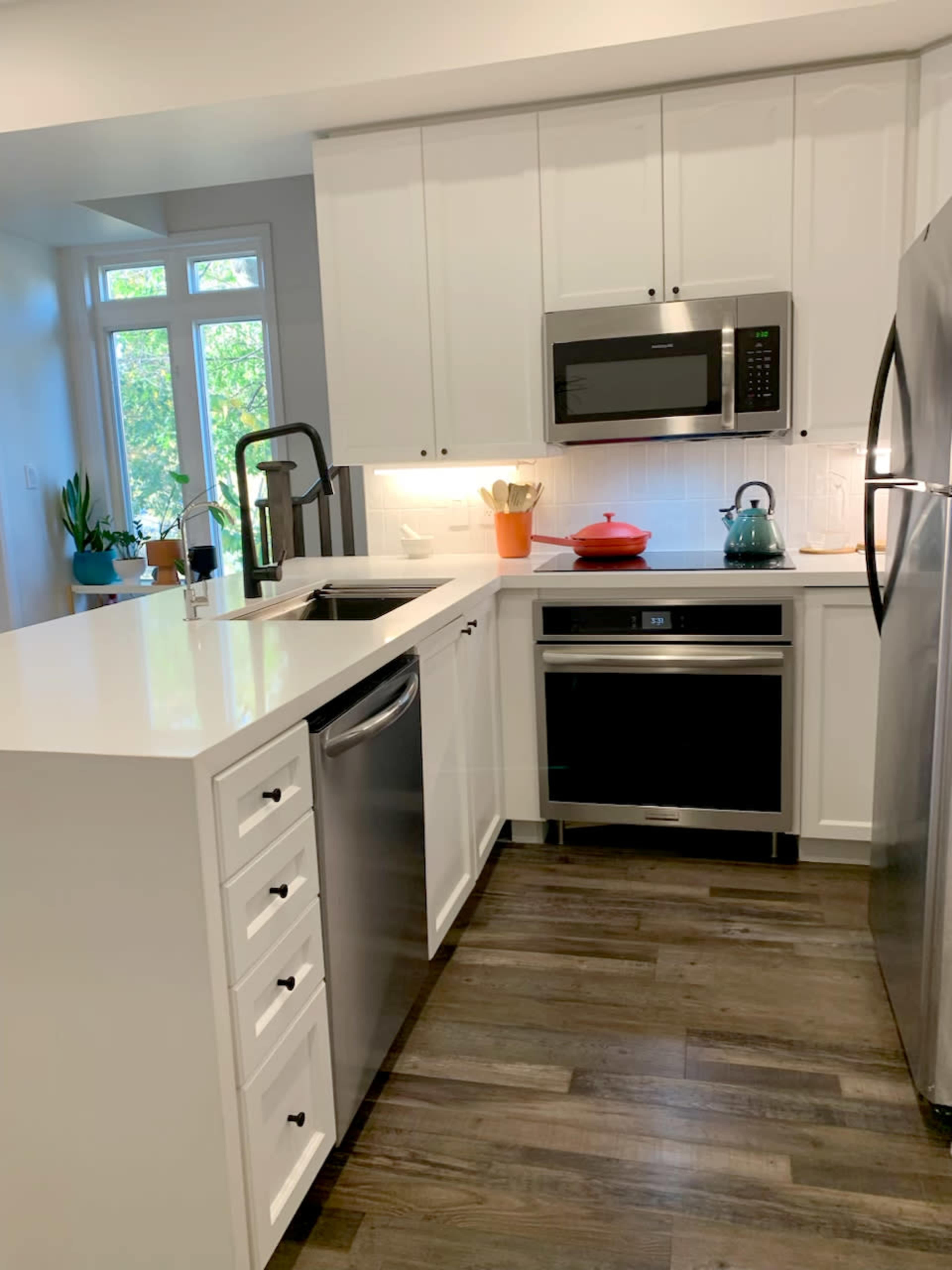The image shows a modern kitchen featuring white cabinetry, stainless steel appliances, and a central island with a sink.