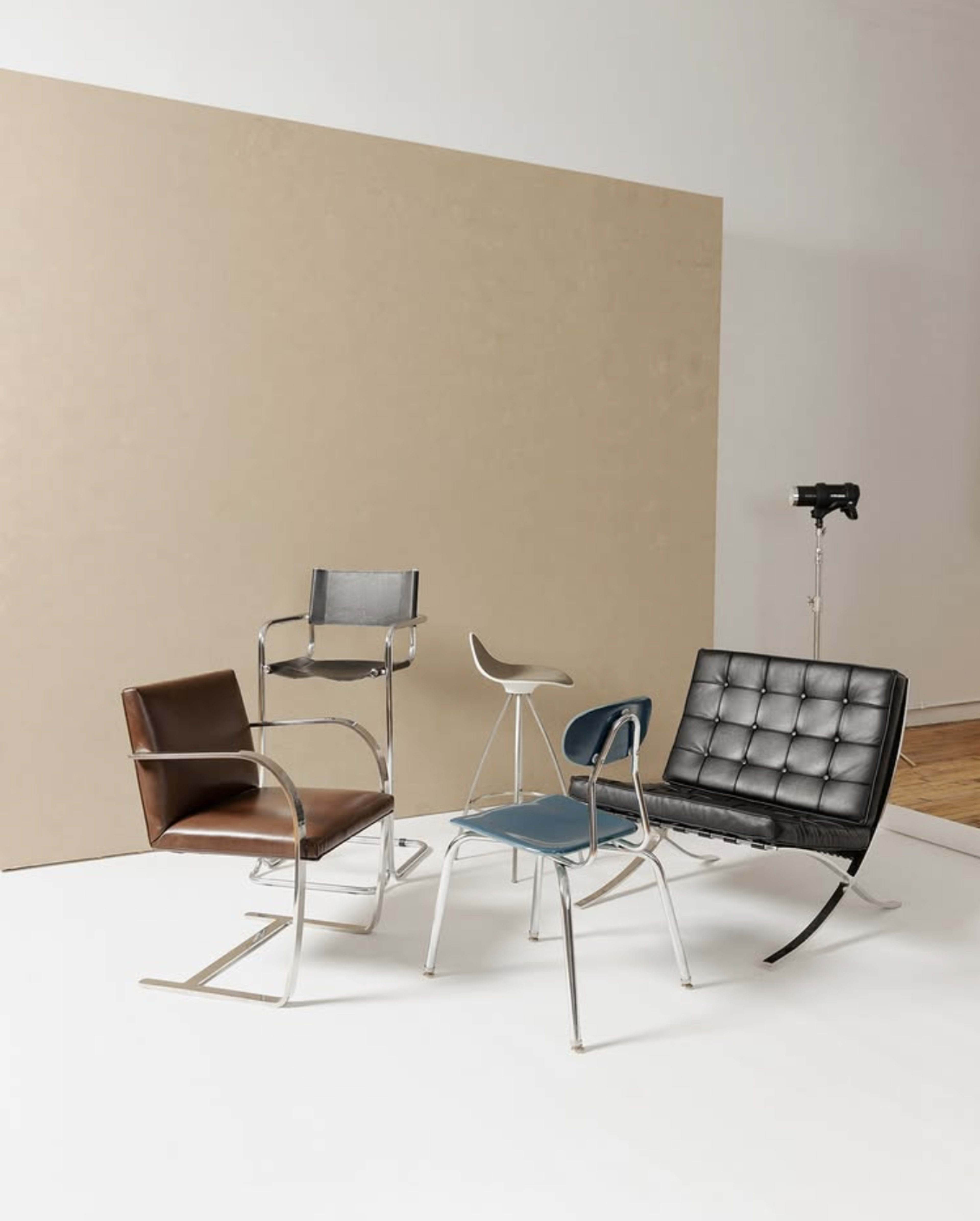 The image features four distinct chairs arranged in a minimalist setting with a plain backdrop.