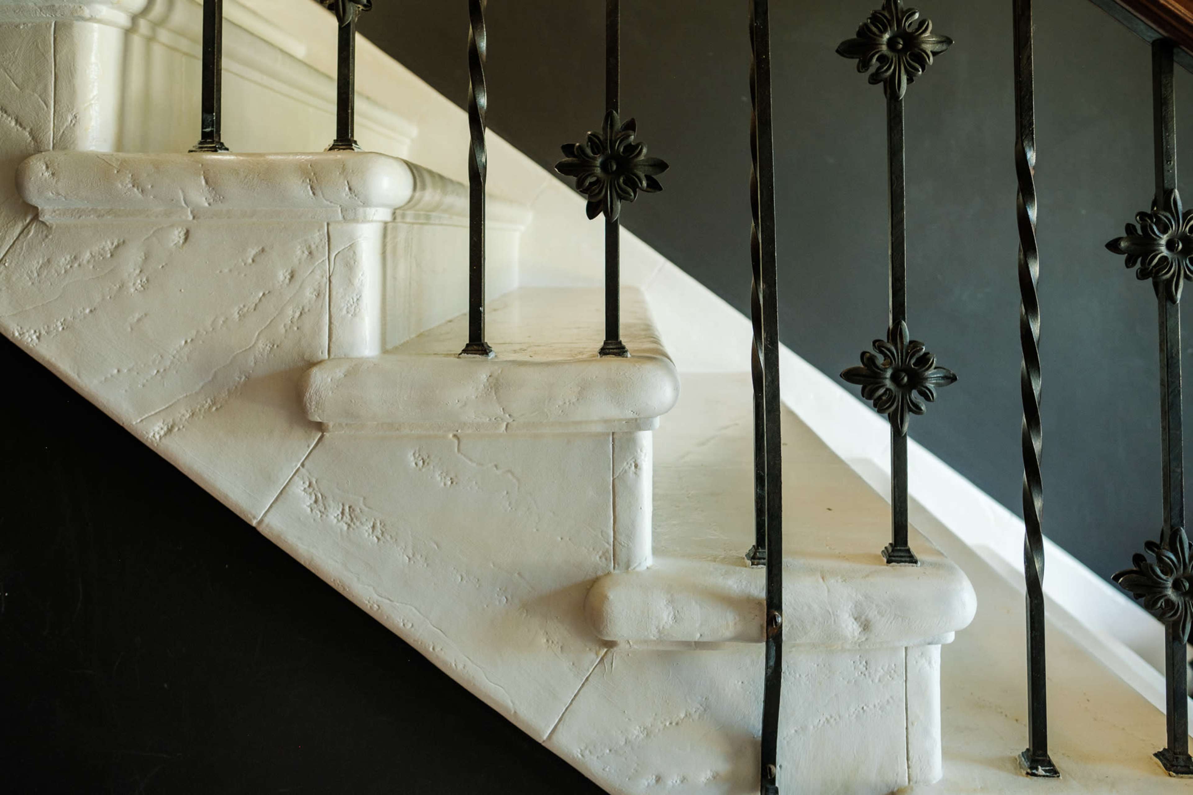 A set of white stone stairs ascends against a dark wall, featuring ornate black railings.