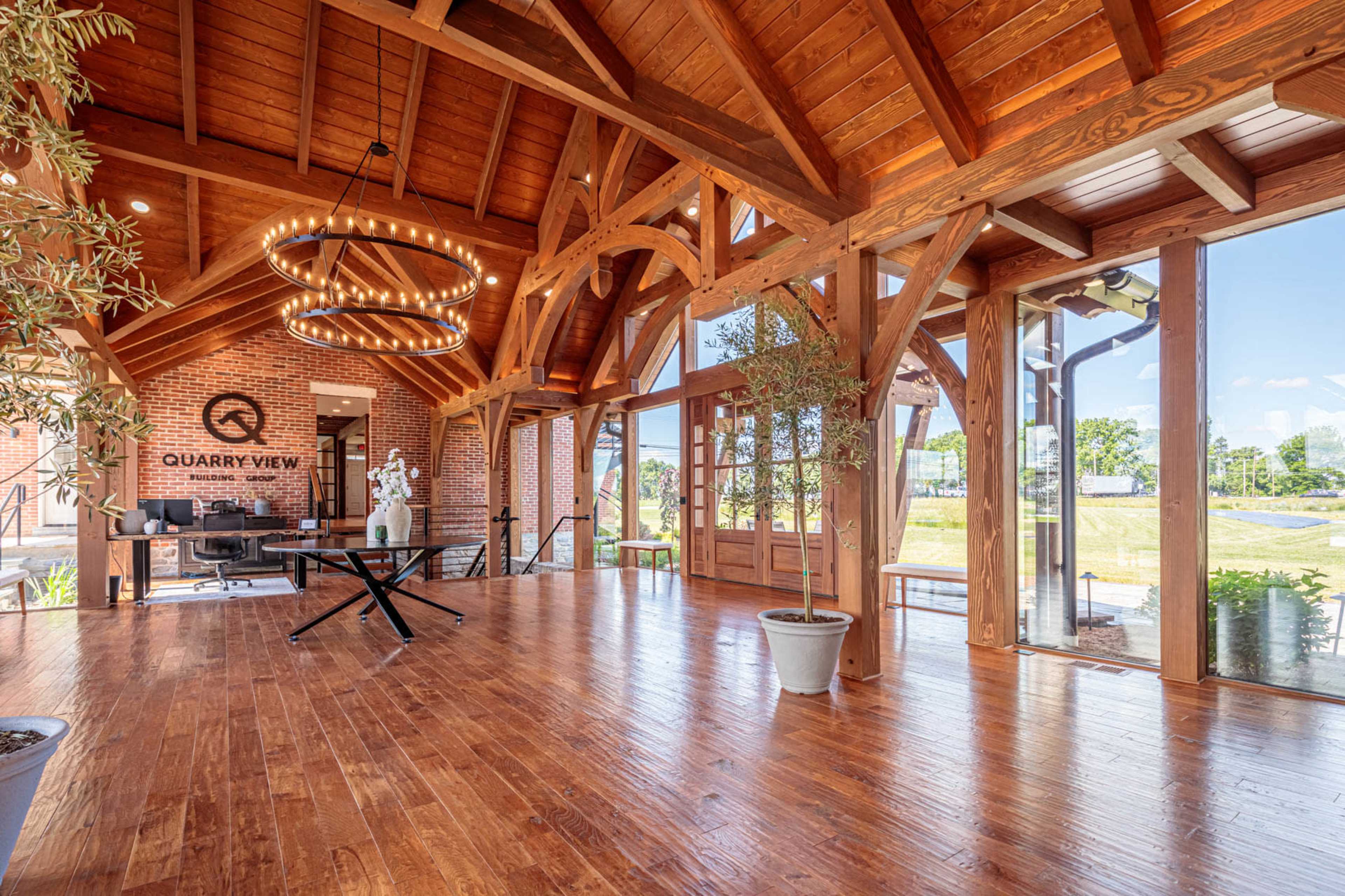A spacious interior with wooden beams and a polished wooden floor, featuring large windows that provide a view of the outdoors.