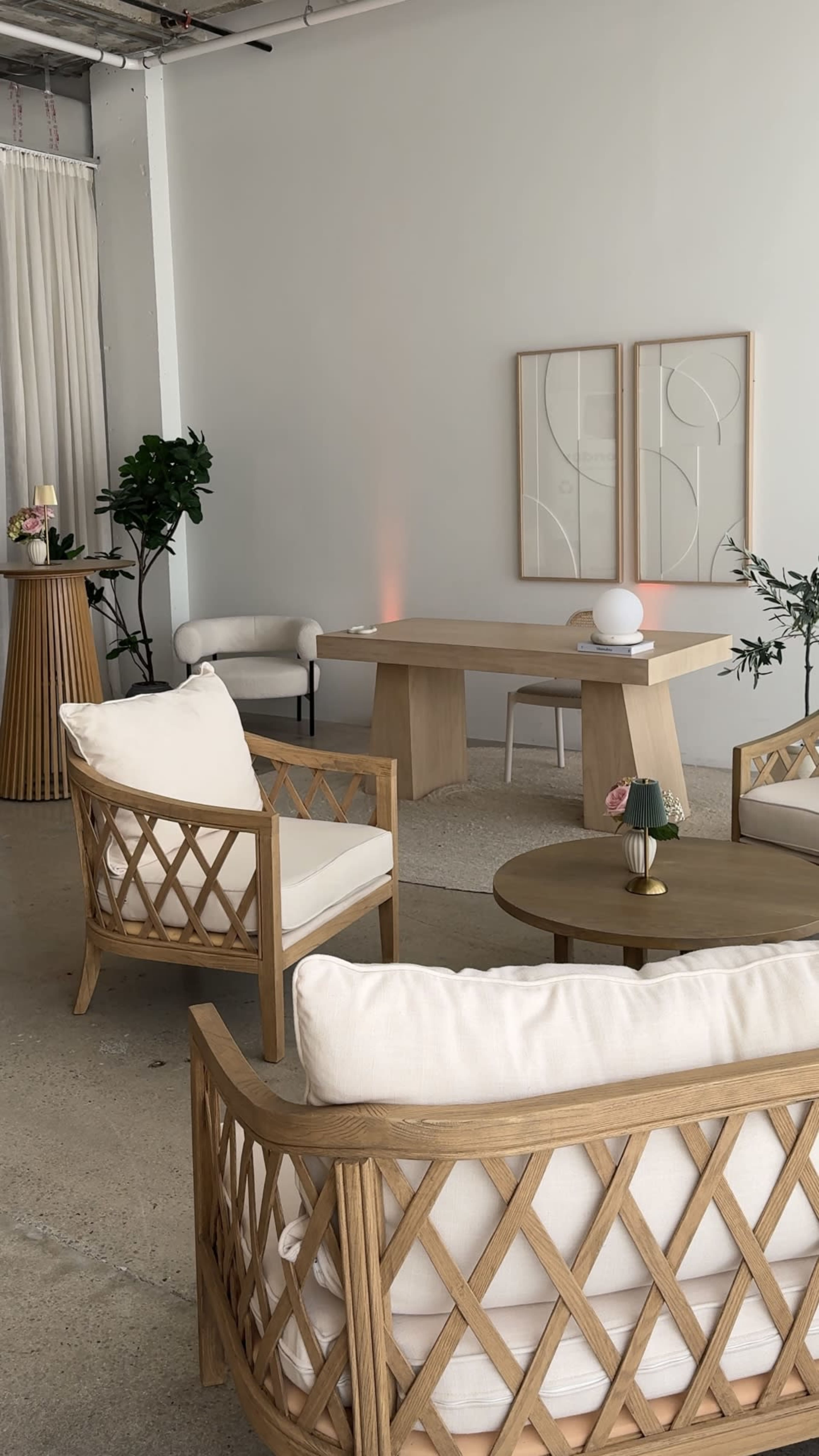 The image shows a modern, minimalistic interior with wooden furniture, a round table, and neutral-colored seating arranged around a low table.