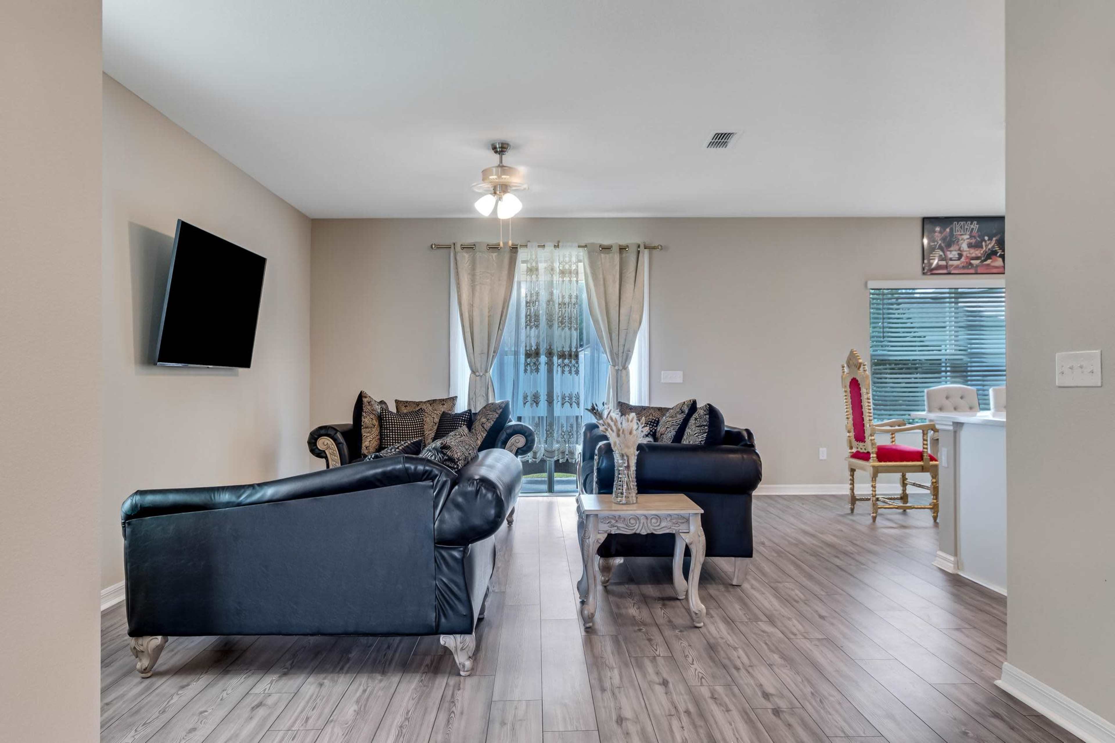 The living room features black leather sofas, a wooden coffee table, and a large window with sheer curtains.