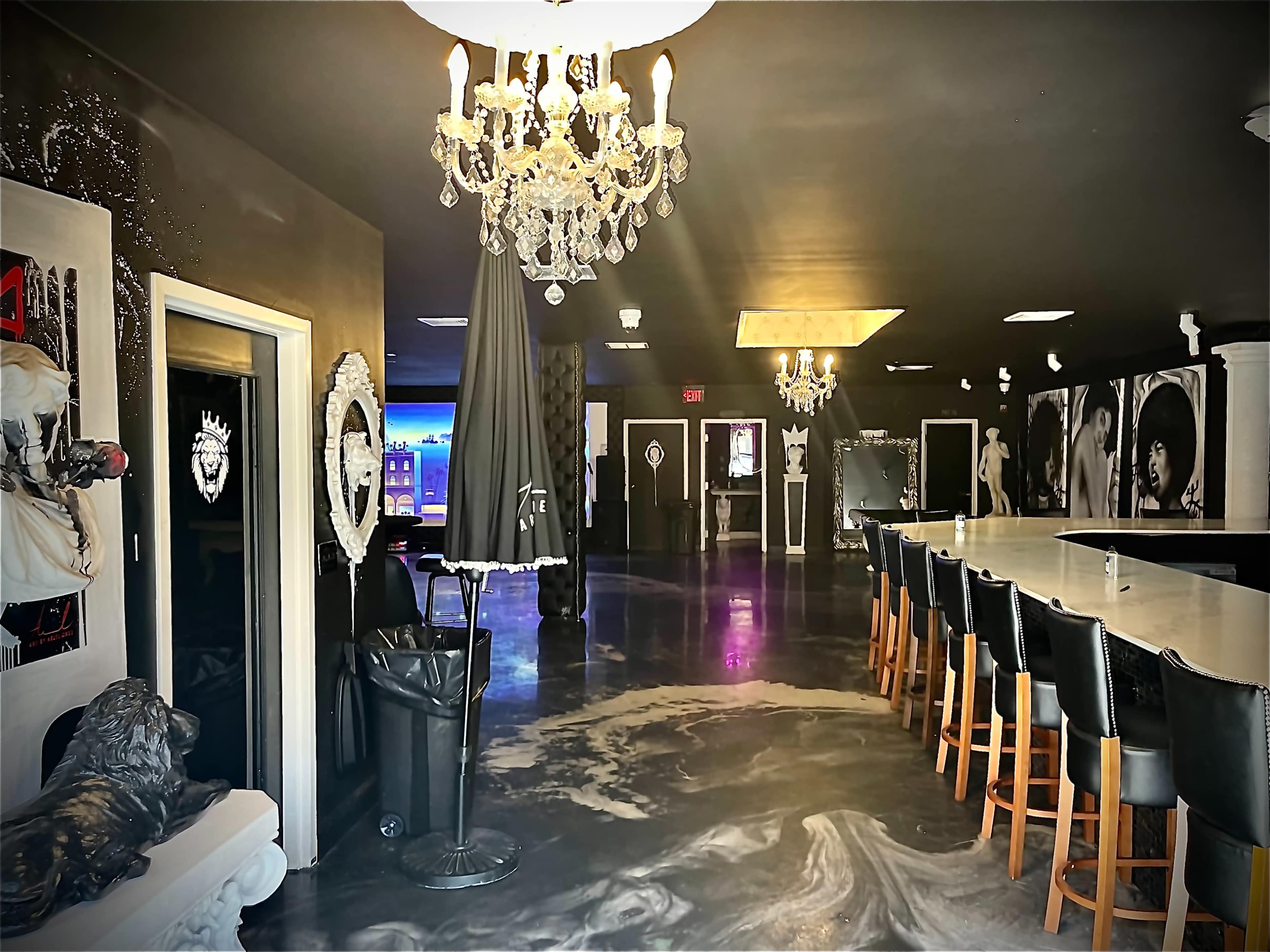 A sleek, modern bar area featuring a long countertop, ornate chandeliers, and black and white wall decor.