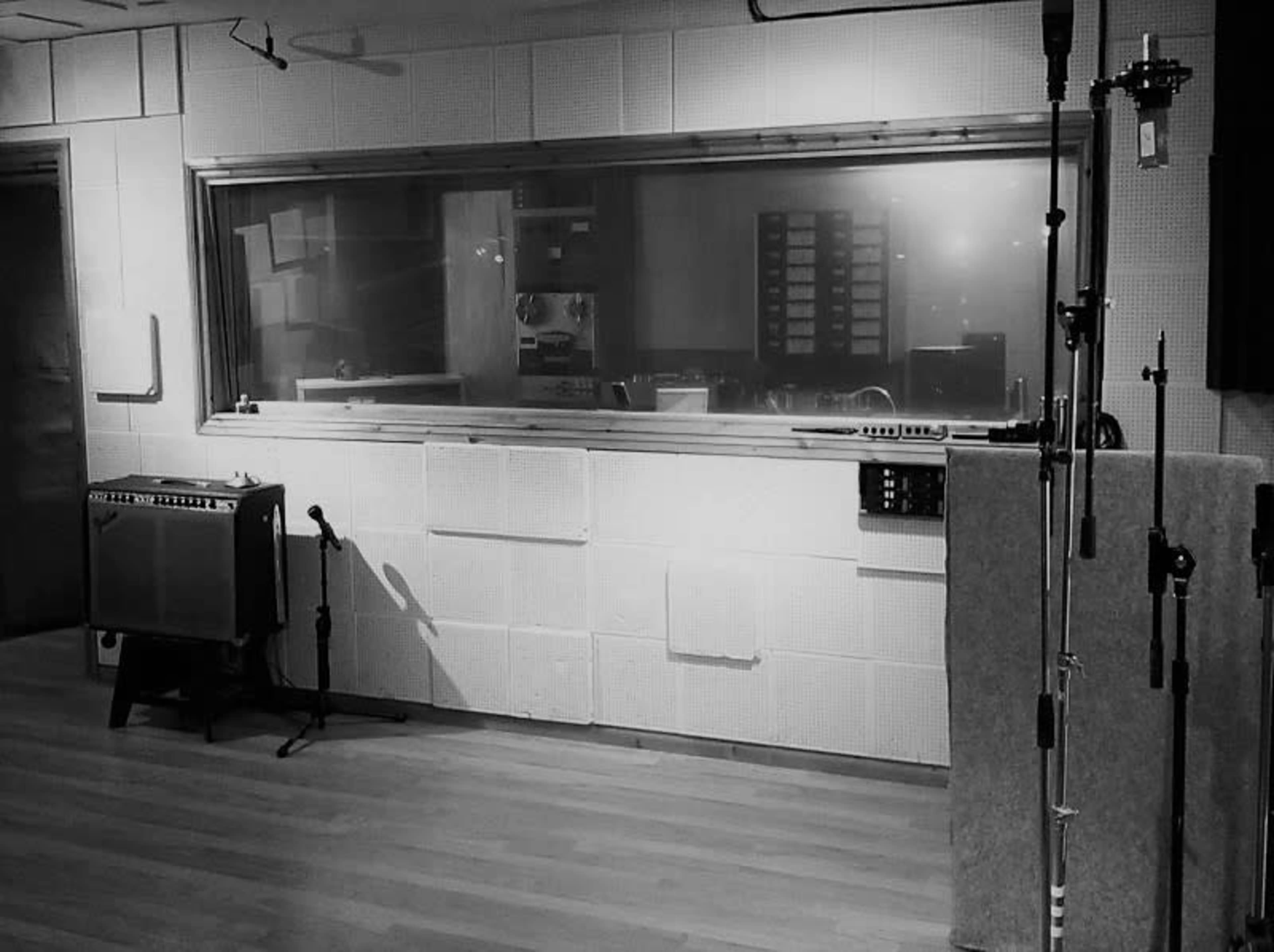 A dimly lit recording studio with soundproofing panels on the walls, a microphone stand, and an amplifier positioned nearby.