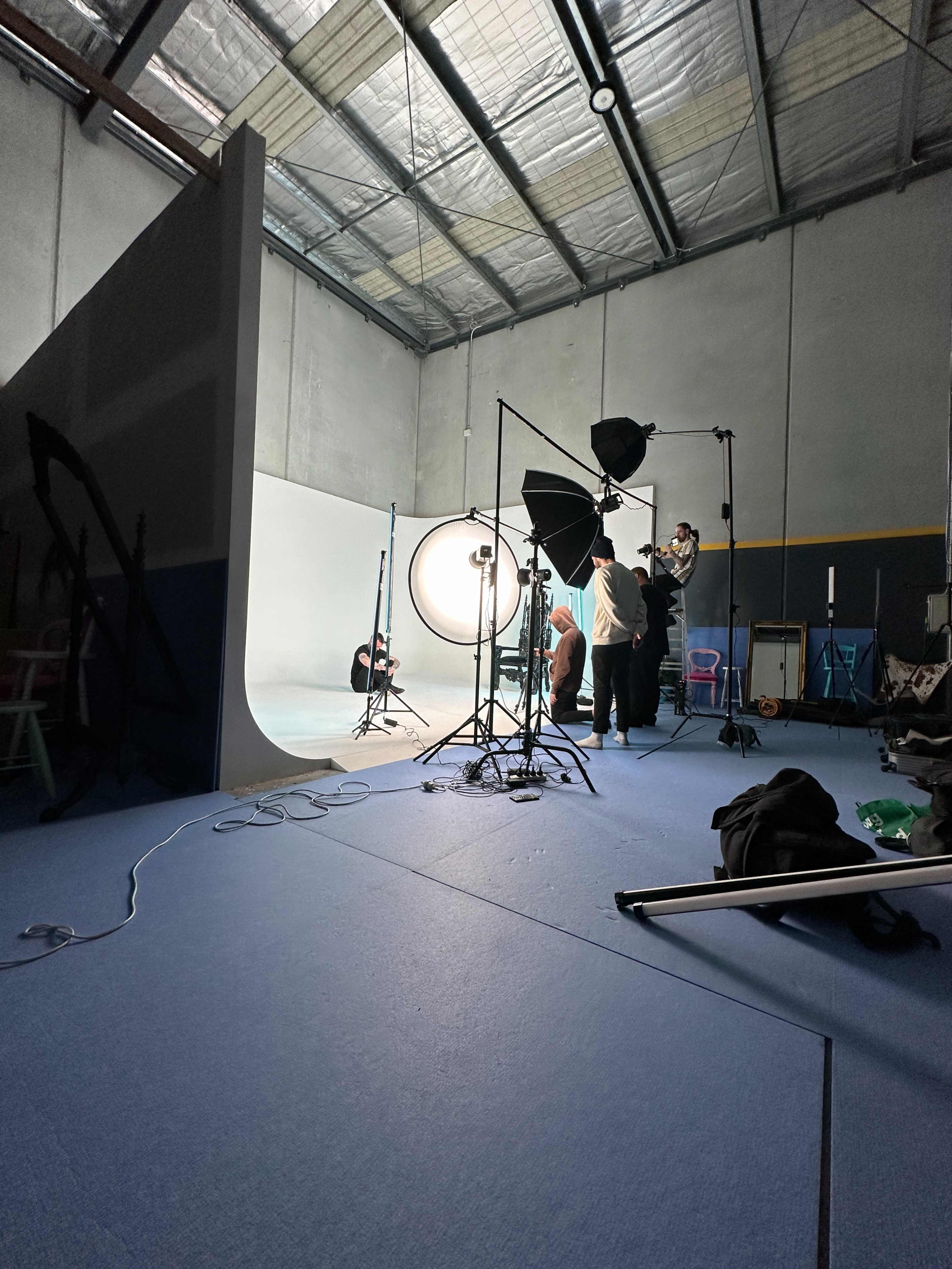 A photography studio is set up with several lights, backdrops, and individuals preparing for a photoshoot.
