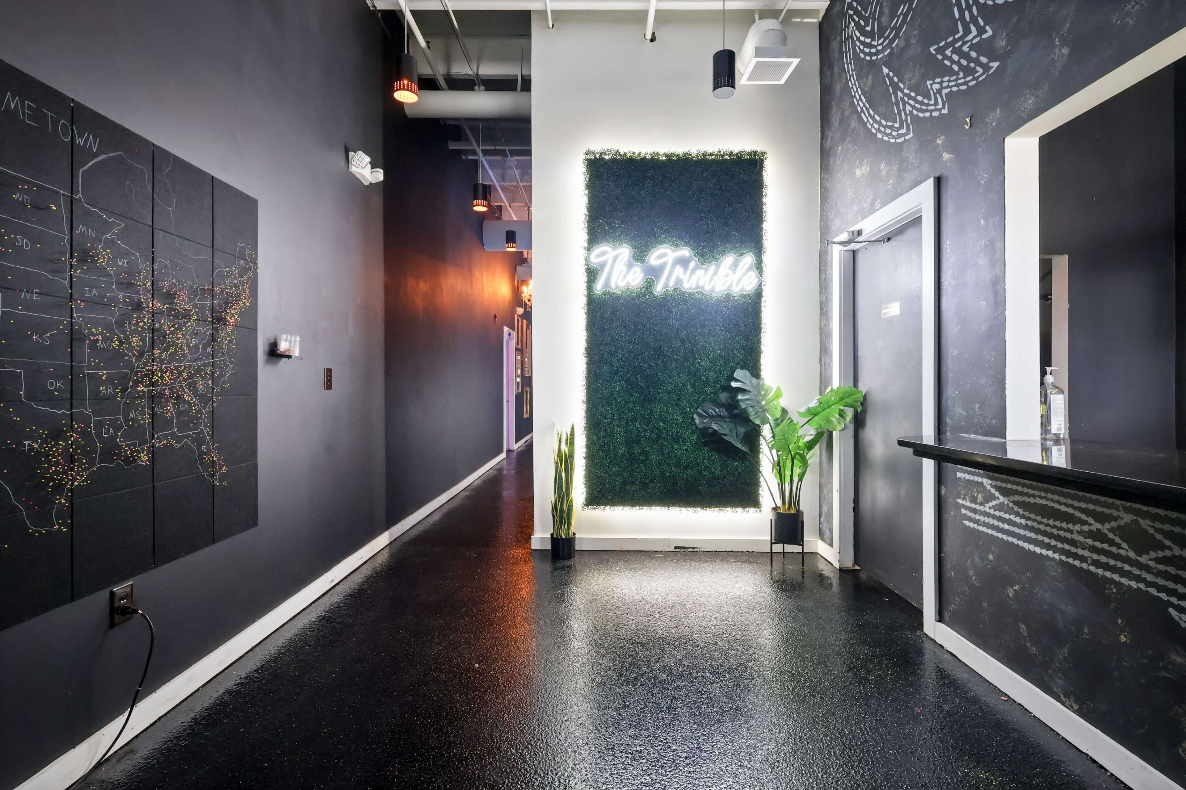 The image shows a narrow hallway with dark walls, a large map on one side, and a green living wall with the phrase "No Trouble" illuminated on the other.