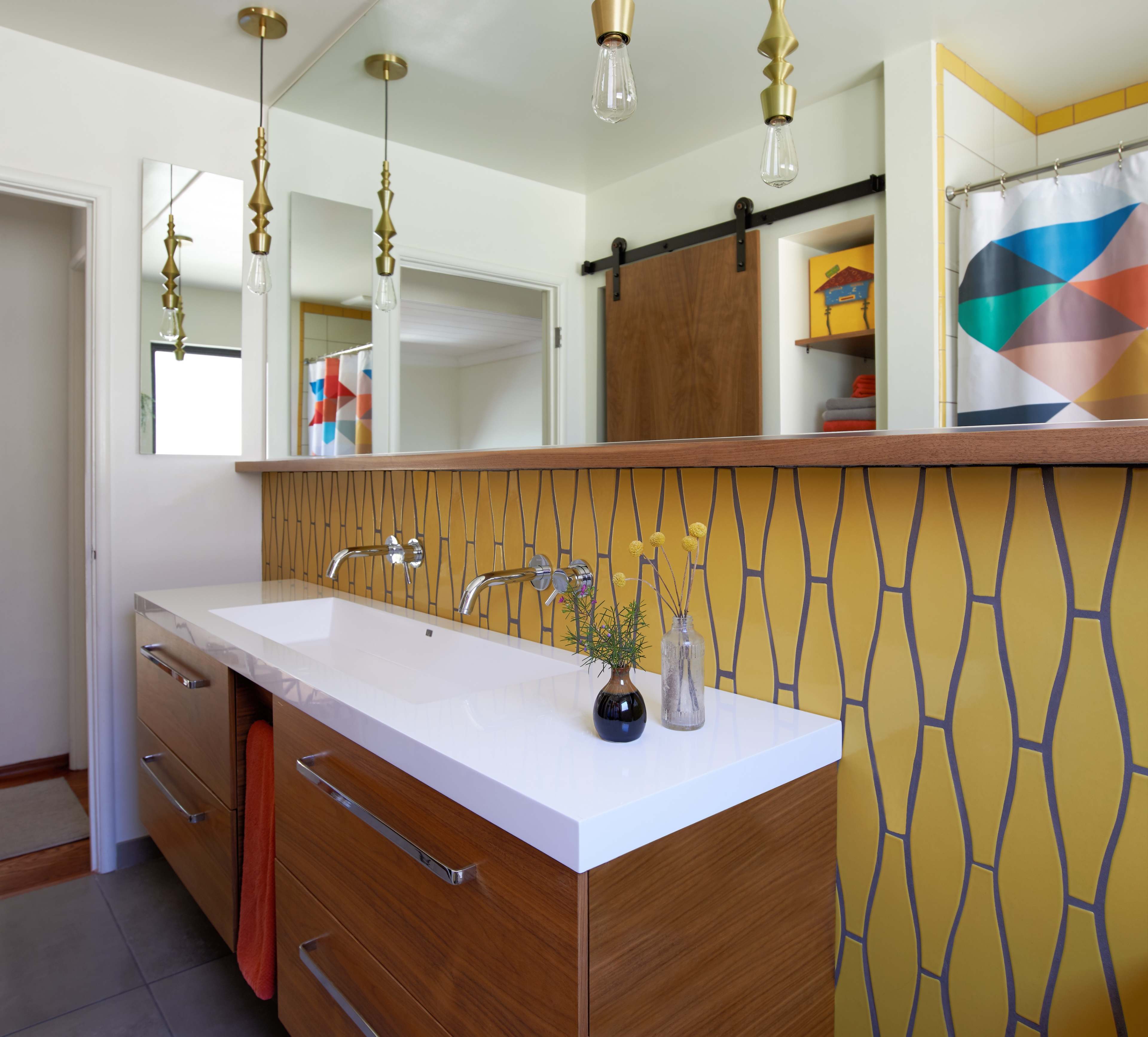 A modern bathroom features a double vanity with a white countertop, wooden cabinetry, and yellow geometric tile accents on the wall.