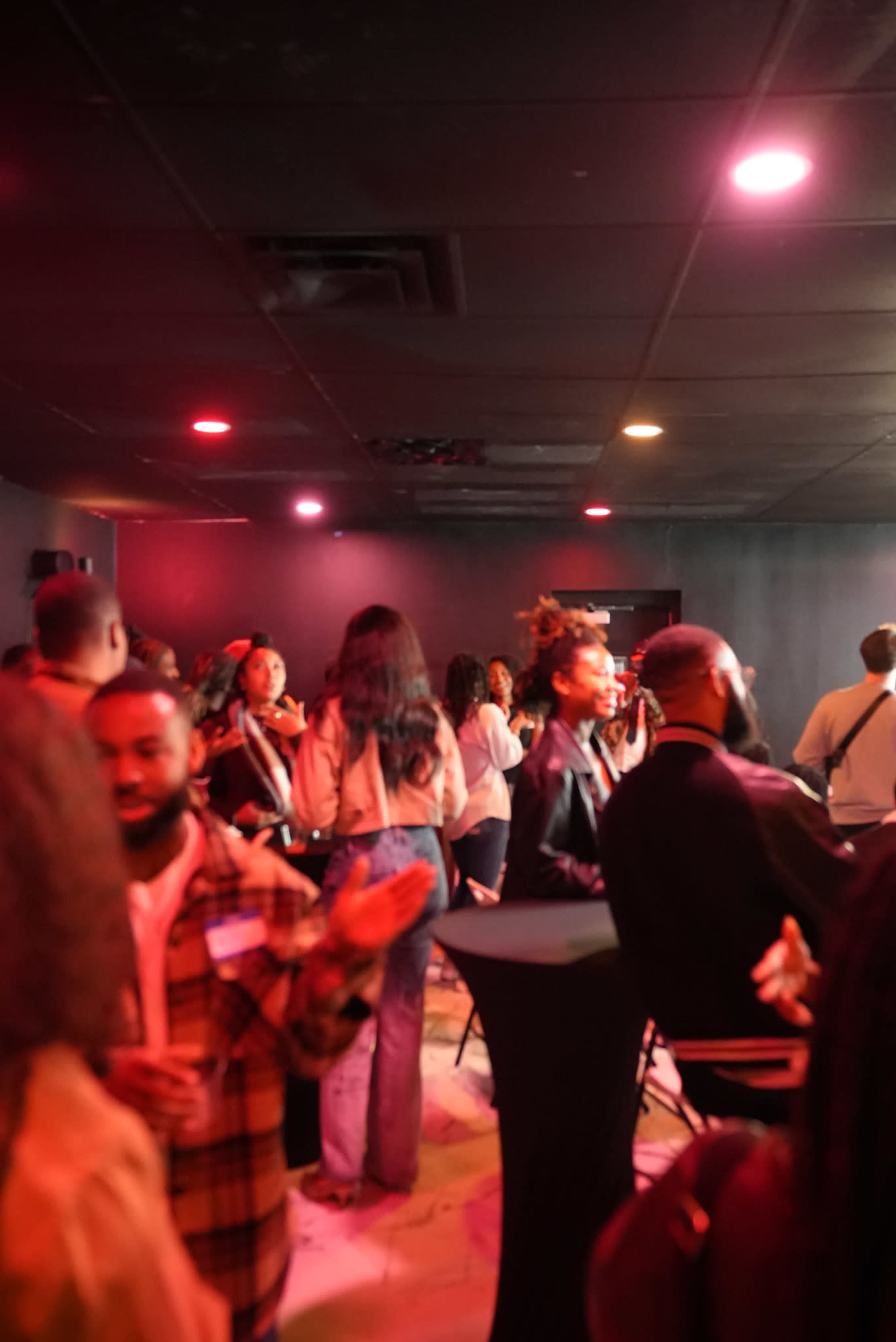 A group of people socialize in a dimly lit room with colorful lights.