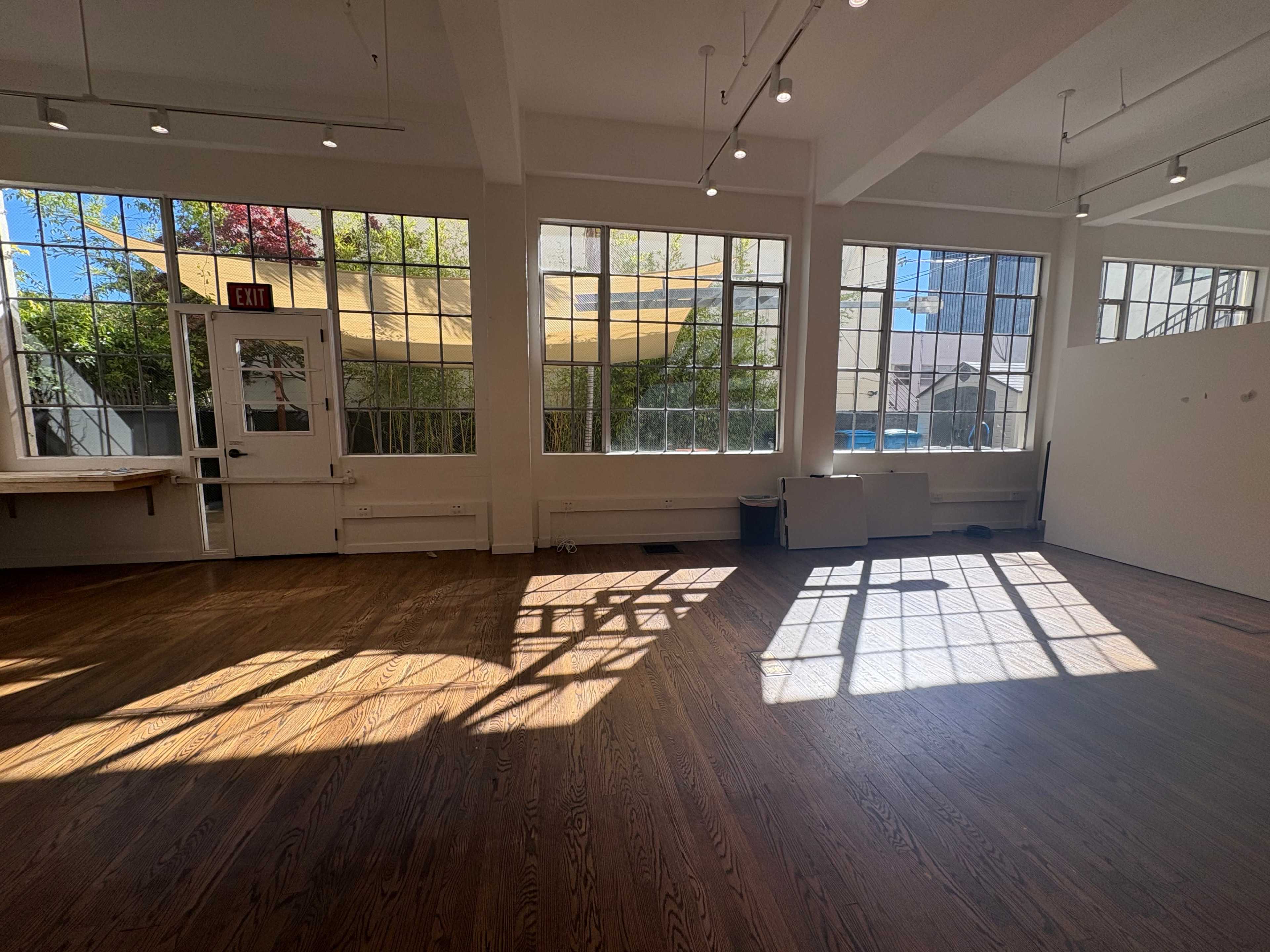 The image shows a bright interior space featuring large windows that allow natural light to illuminate the wooden floor.