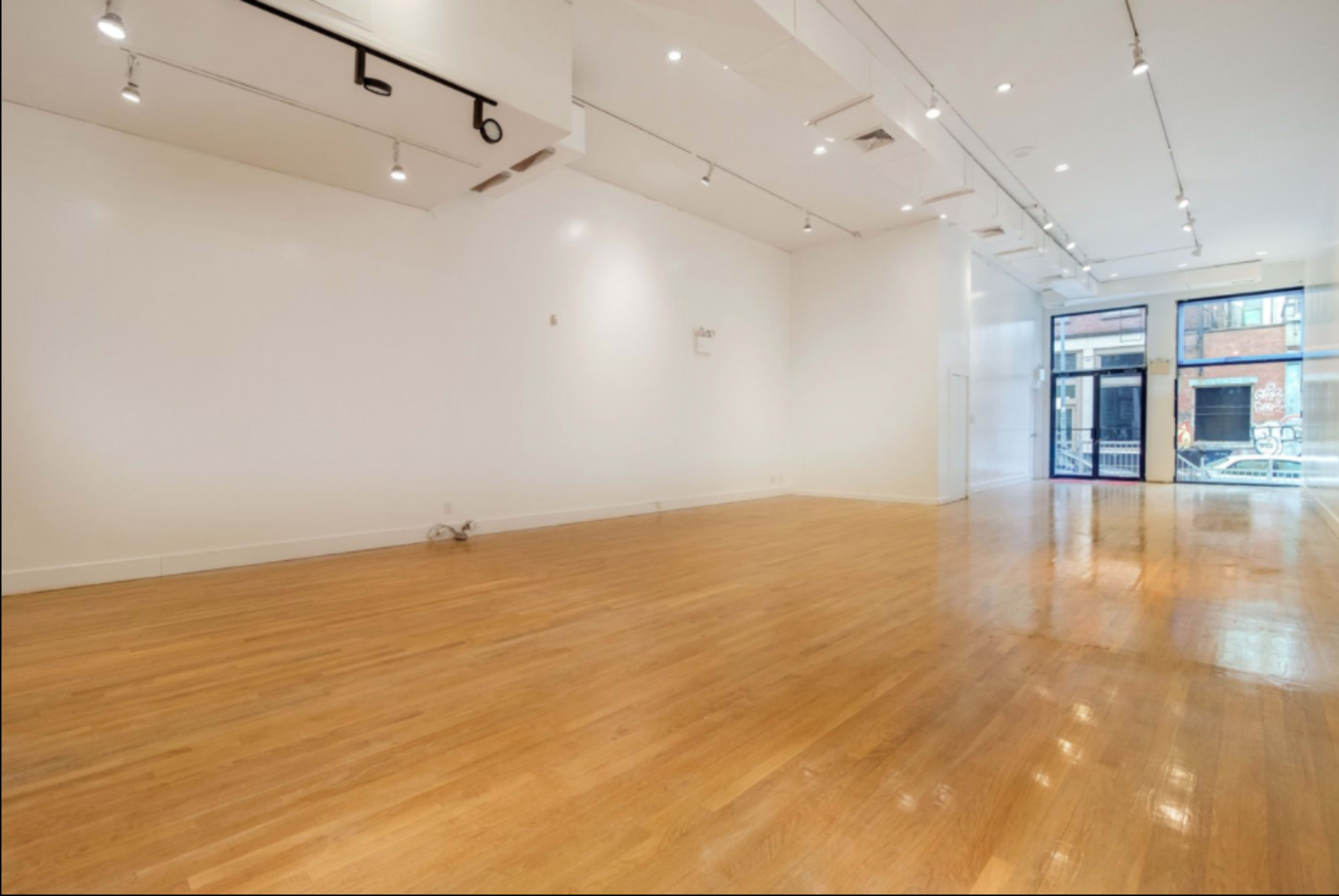 A spacious, empty interior room with hardwood floors and large windows facing a street.
