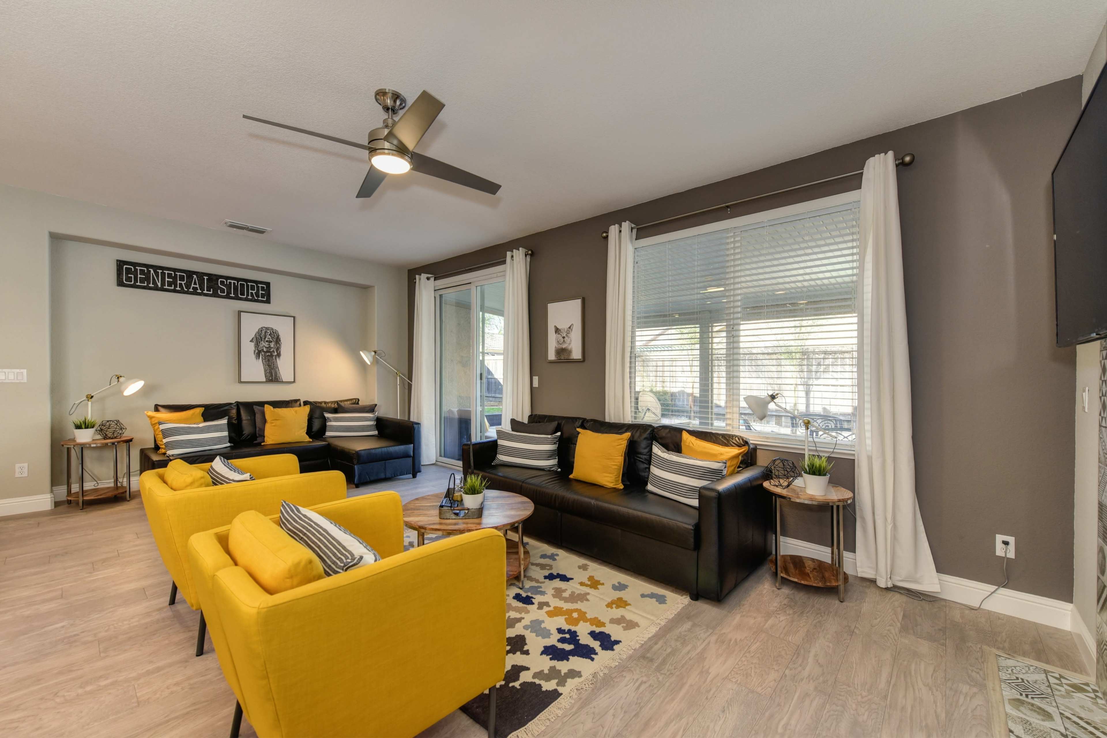 A modern living room features a mix of black and yellow furniture, large windows, and a neutral color scheme with decorative items.