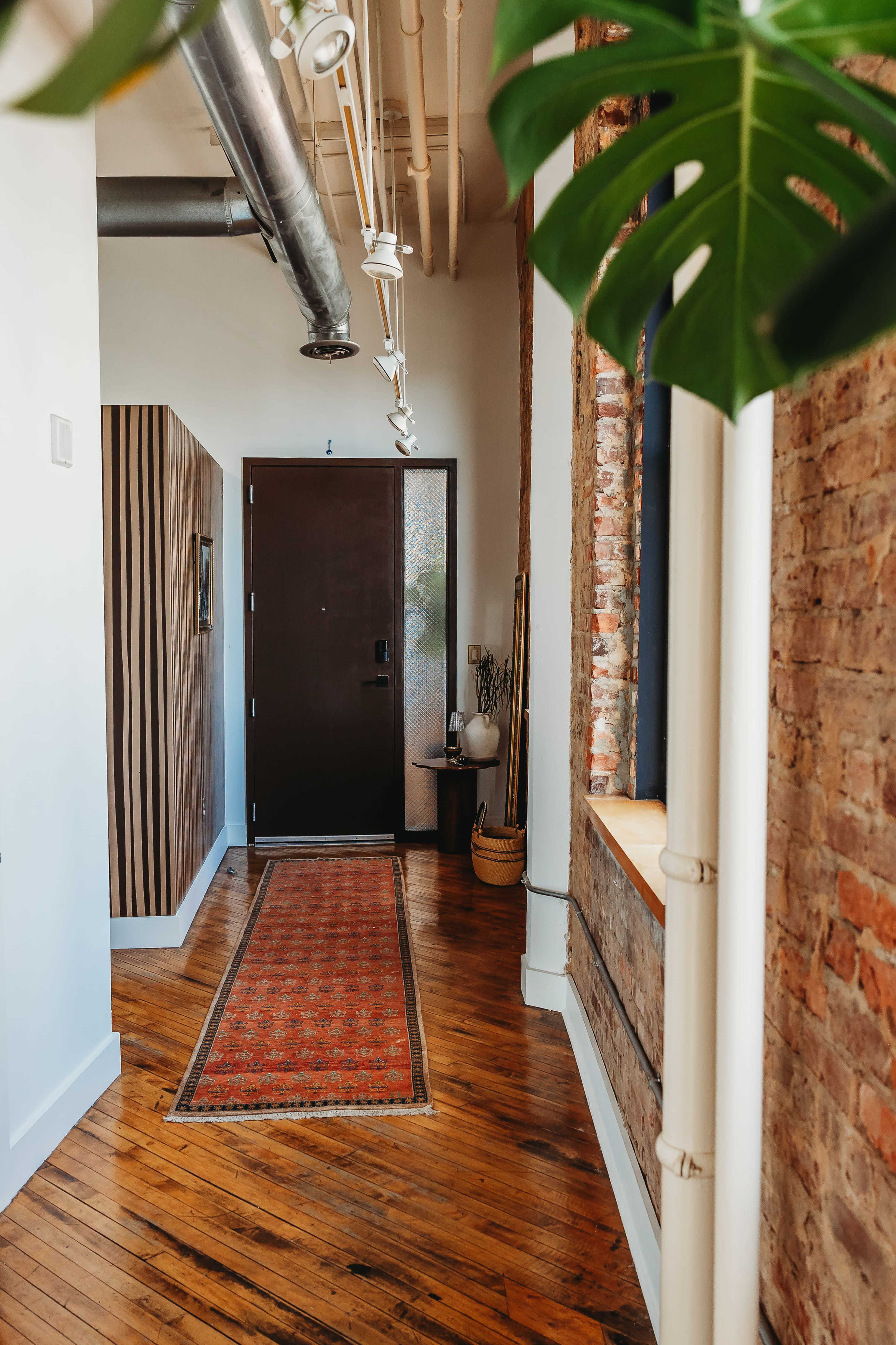 A narrow hallway features a dark door at the end, flanked by a patterned rug and exposed brick walls.