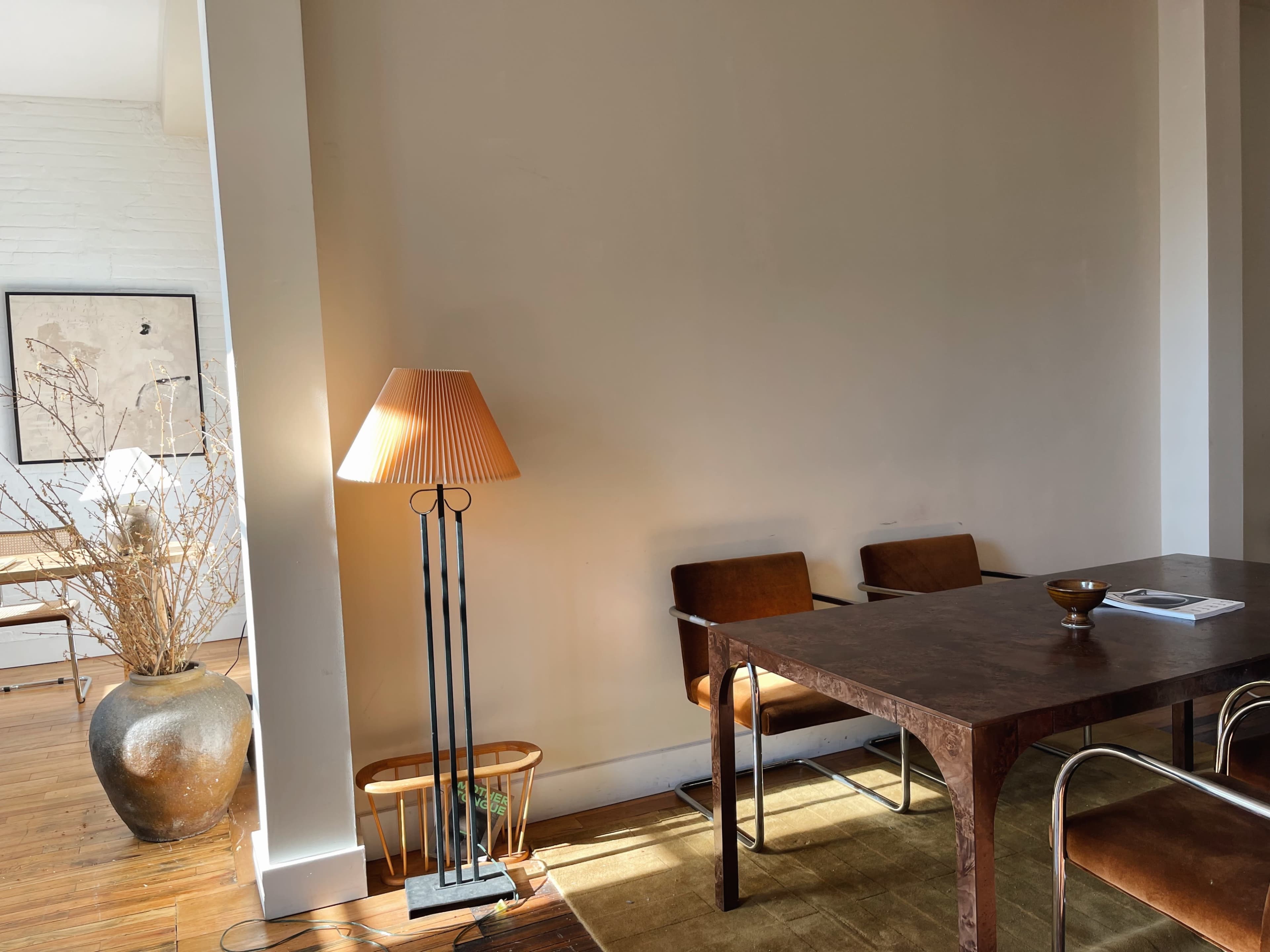 A wooden table with metal chairs is positioned in a well-lit room featuring a floor lamp and decorative plants.