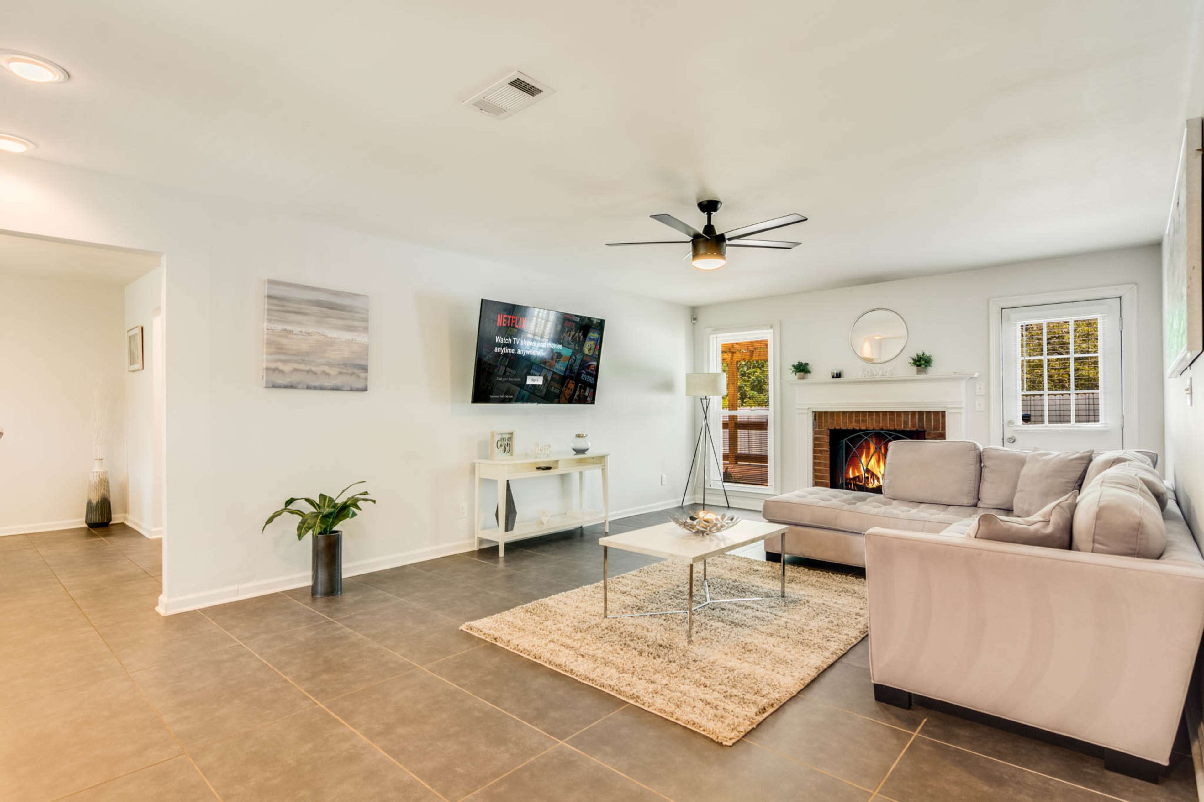 The living room features a sectional sofa, a wall-mounted television, a fireplace, and a coffee table on a beige rug.
