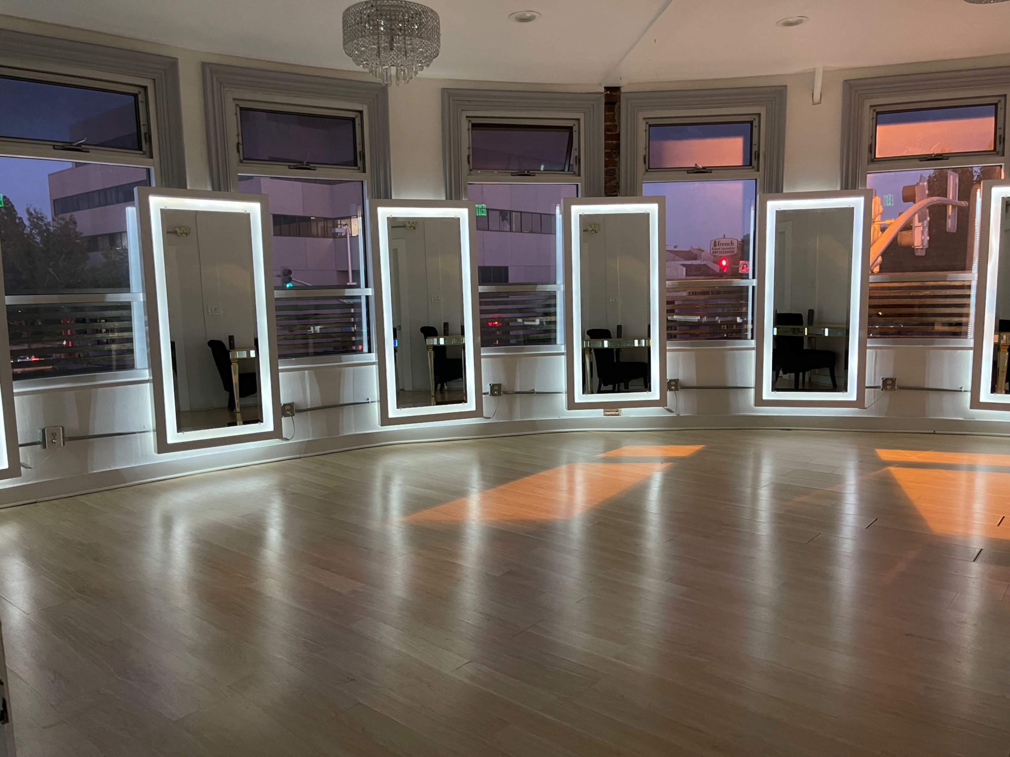 The image shows a room with five illuminated mirrors surrounded by large windows, reflecting the soft light of the setting sun.