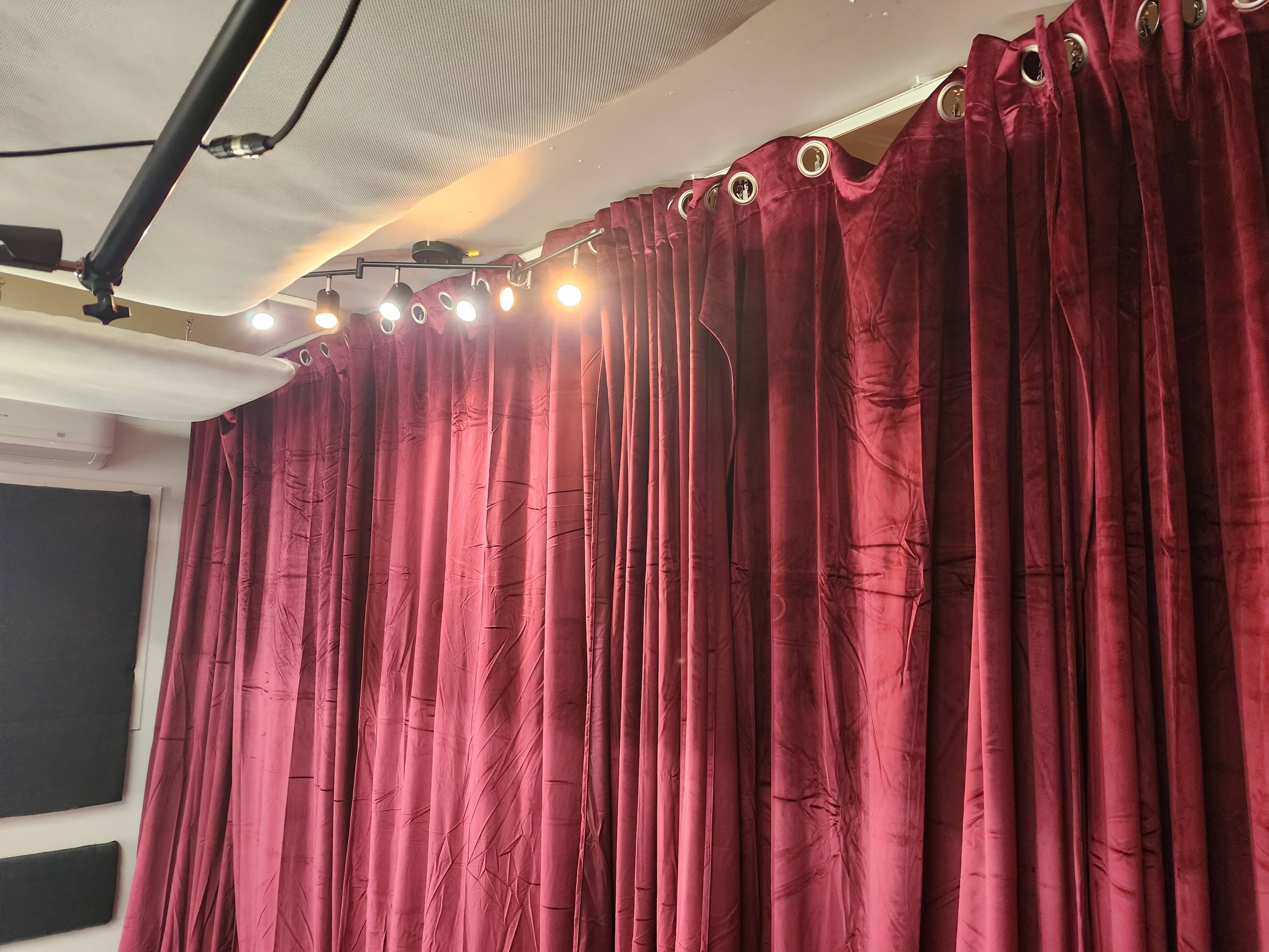 A corner of a room with red velvet curtains and overhead lights illuminating the fabric.