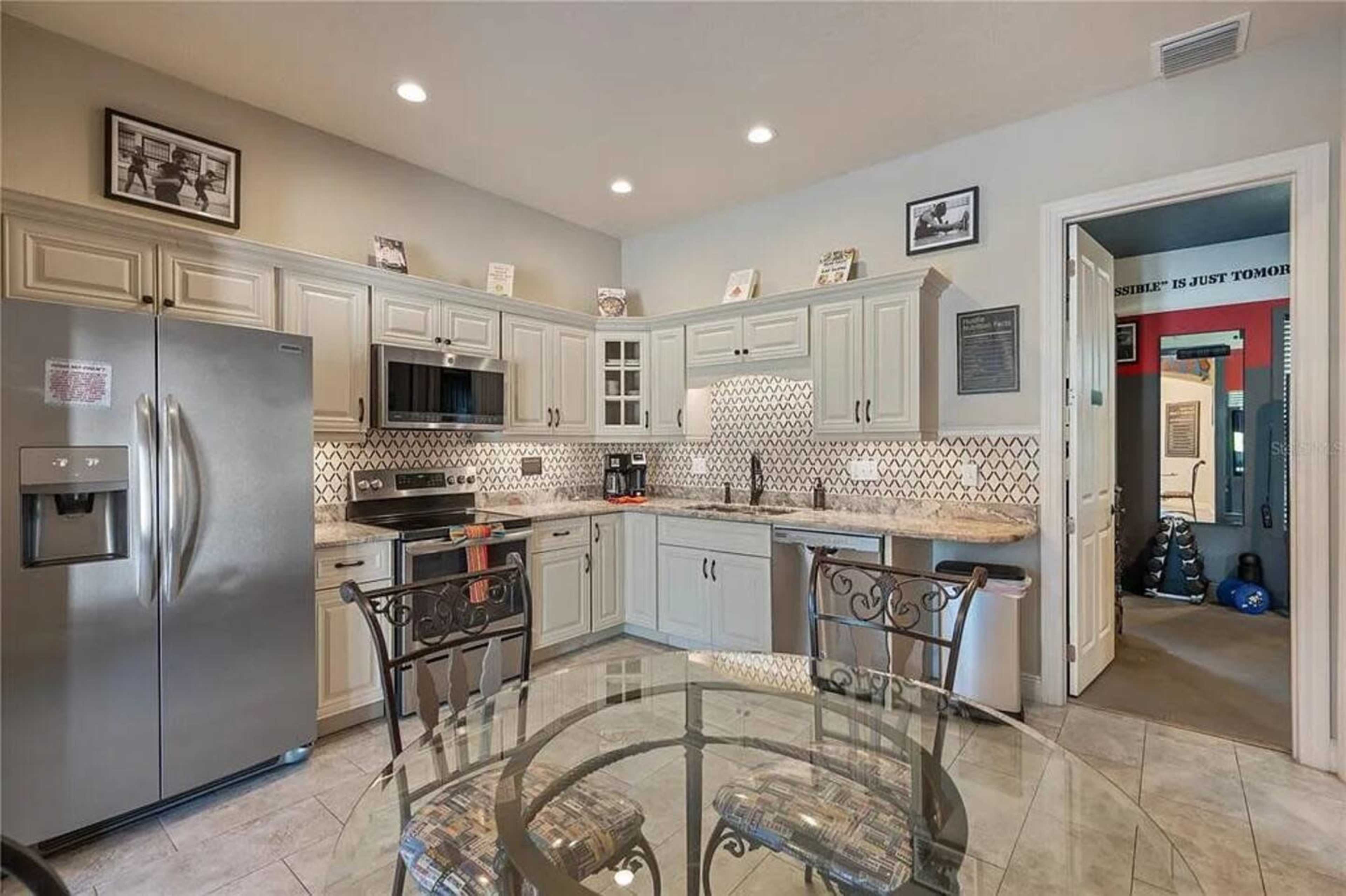 The image shows a modern kitchen with light-colored cabinets, stainless steel appliances, and a dining table in the foreground.