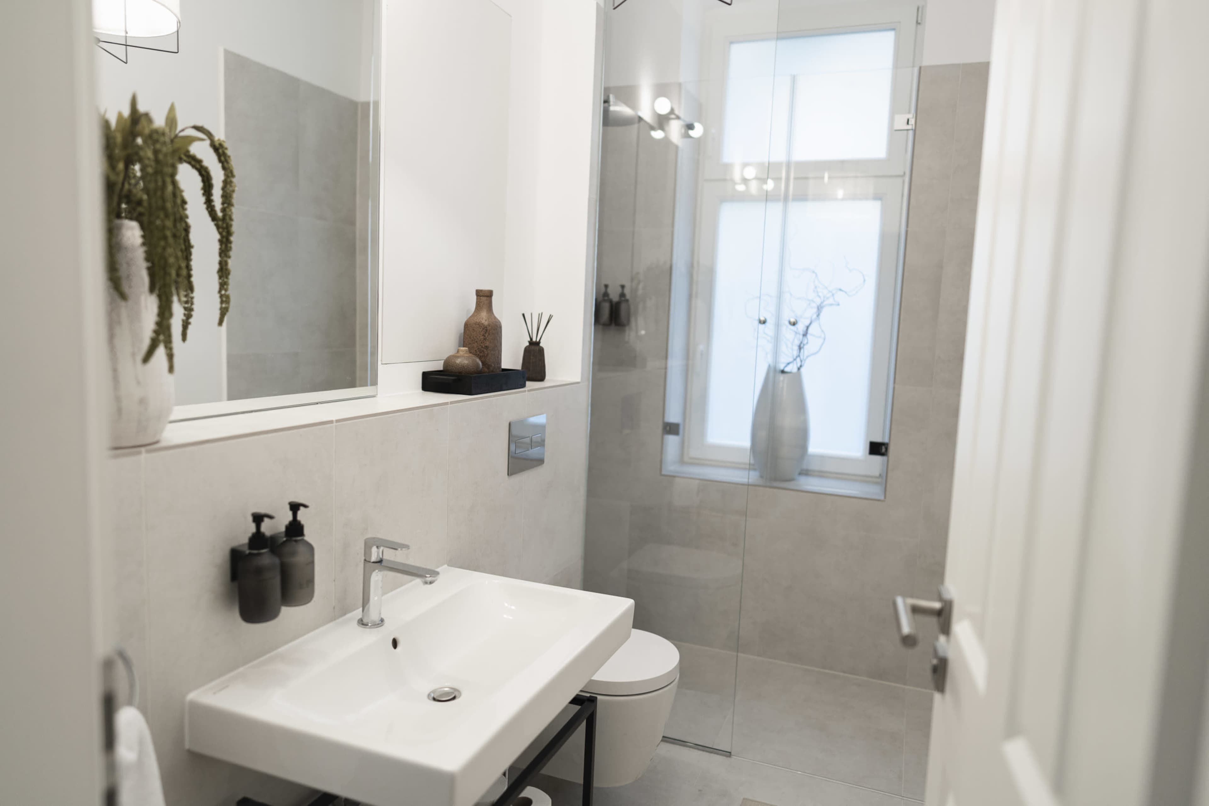 The image shows a modern bathroom featuring a glass shower, a white sink on a black frame, and minimalistic decor.