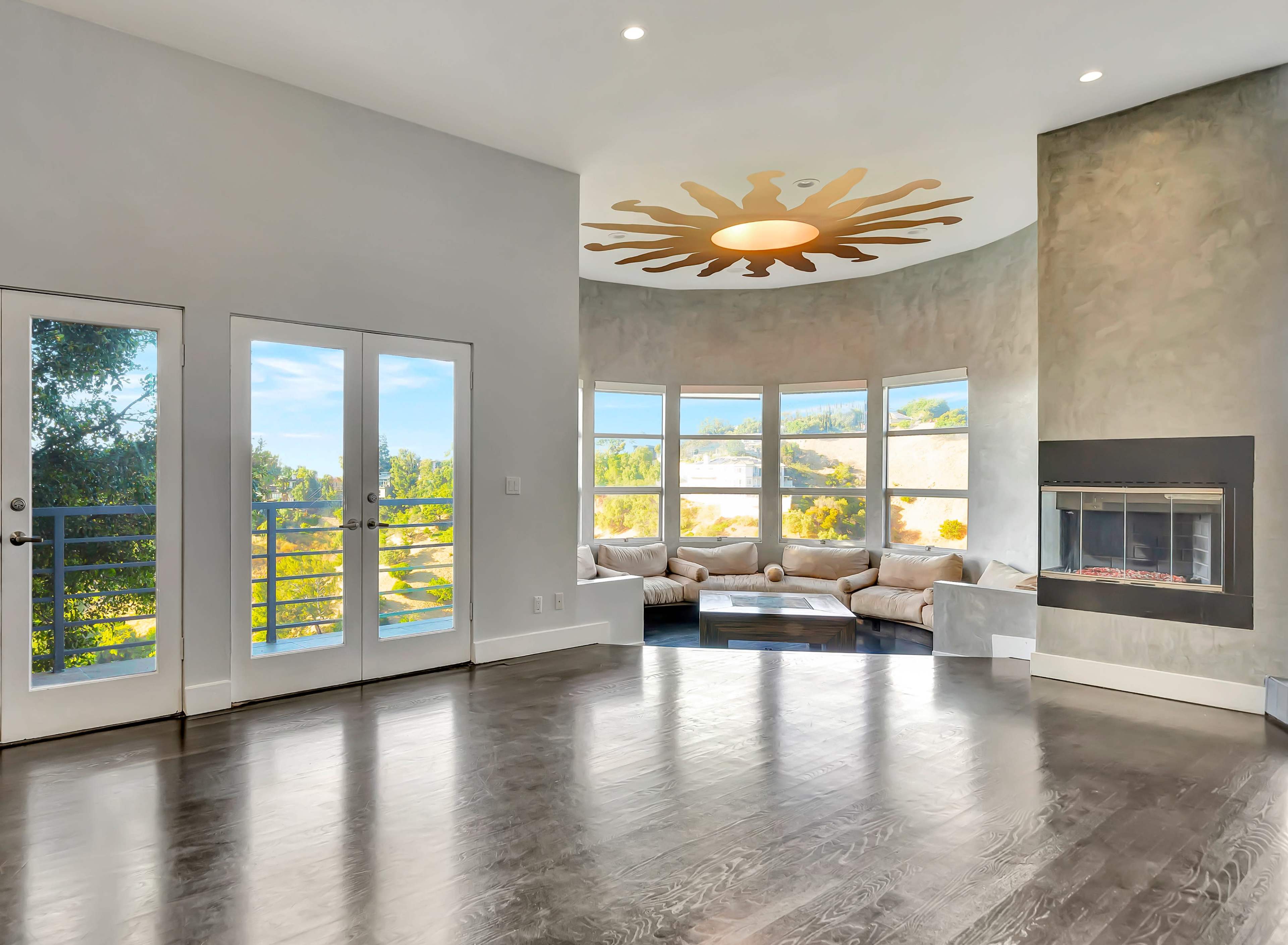 A spacious living room features large windows, a circular ceiling design, a modern fireplace, and access to a patio.