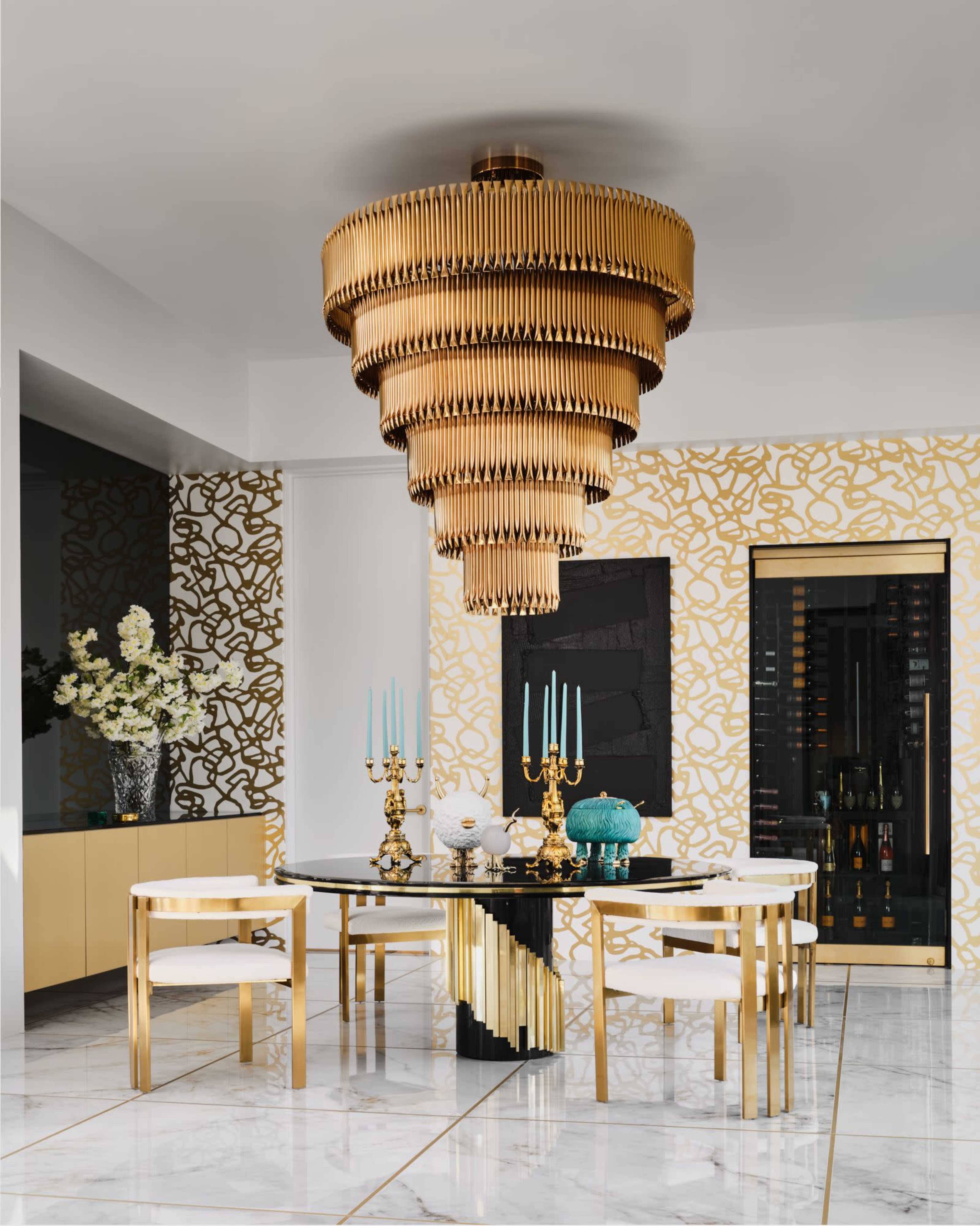 A modern dining room features a large gold chandelier above a black and gold table surrounded by white chairs, with decorative elements including teal candles and vases.