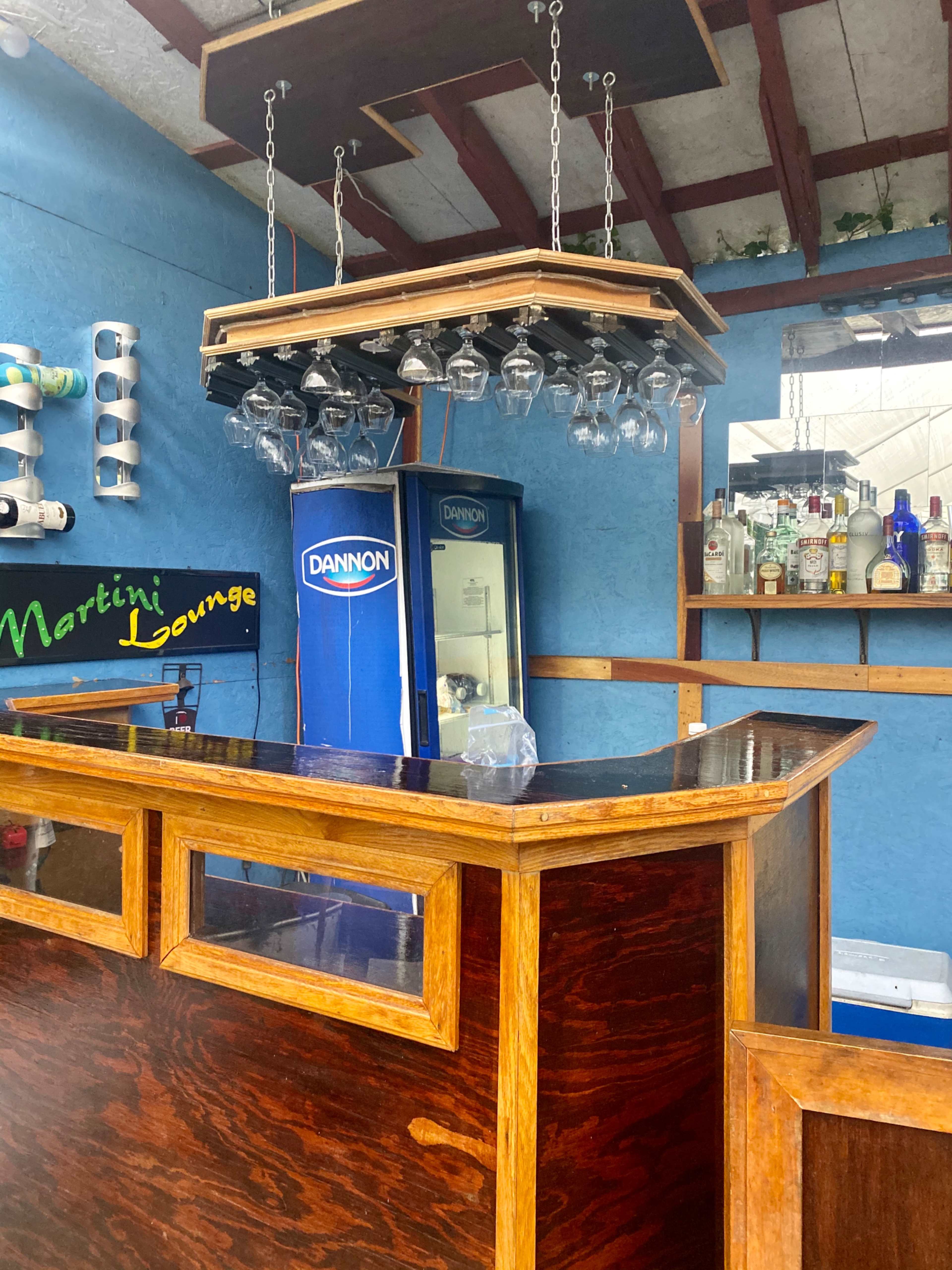 A wooden bar counter with hanging glassware and a refrigerator in a lounge setting.