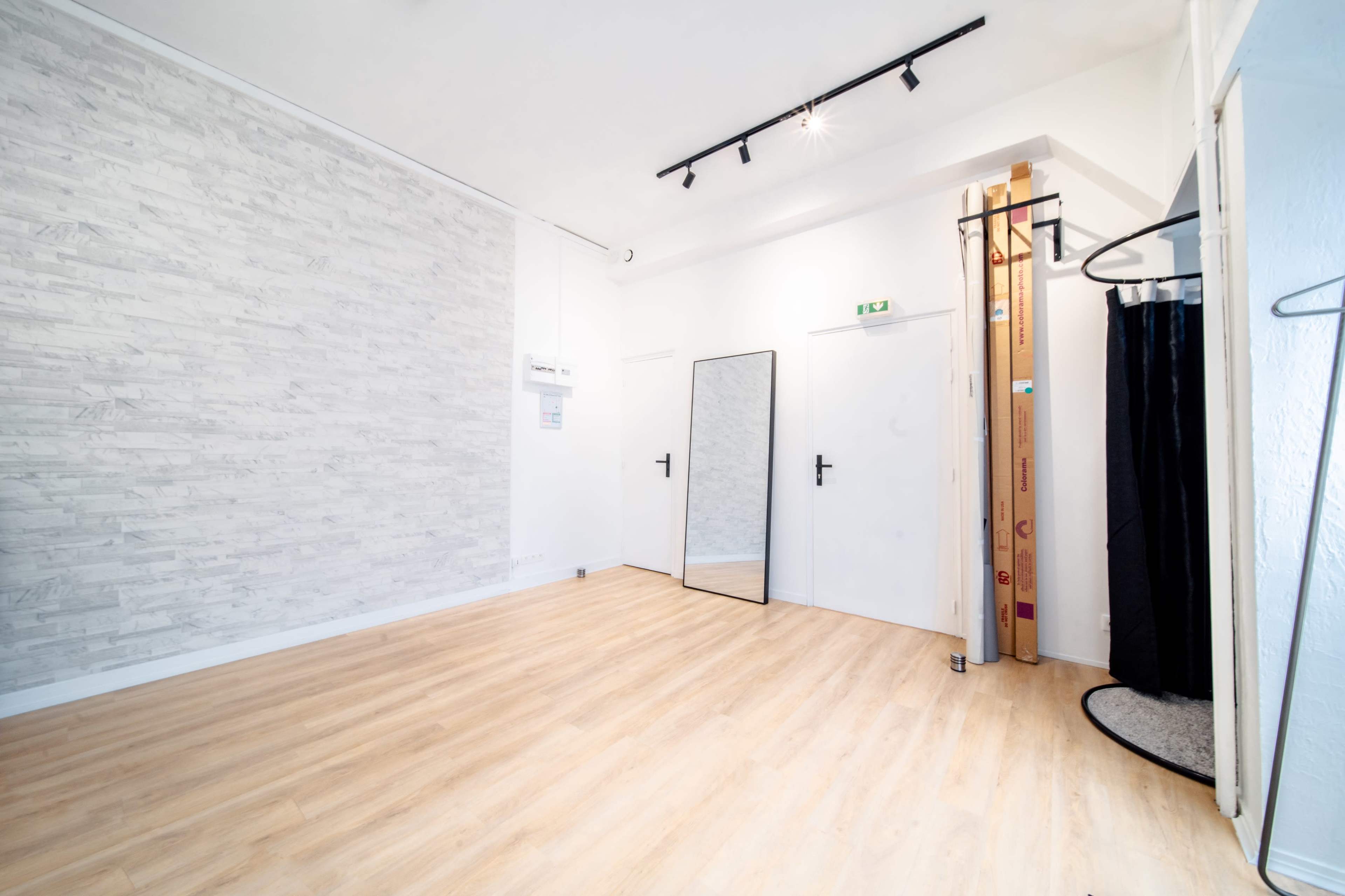 The image shows a spacious room with light wooden flooring, a full-length mirror on one wall, and a small closet space containing wooden panels.