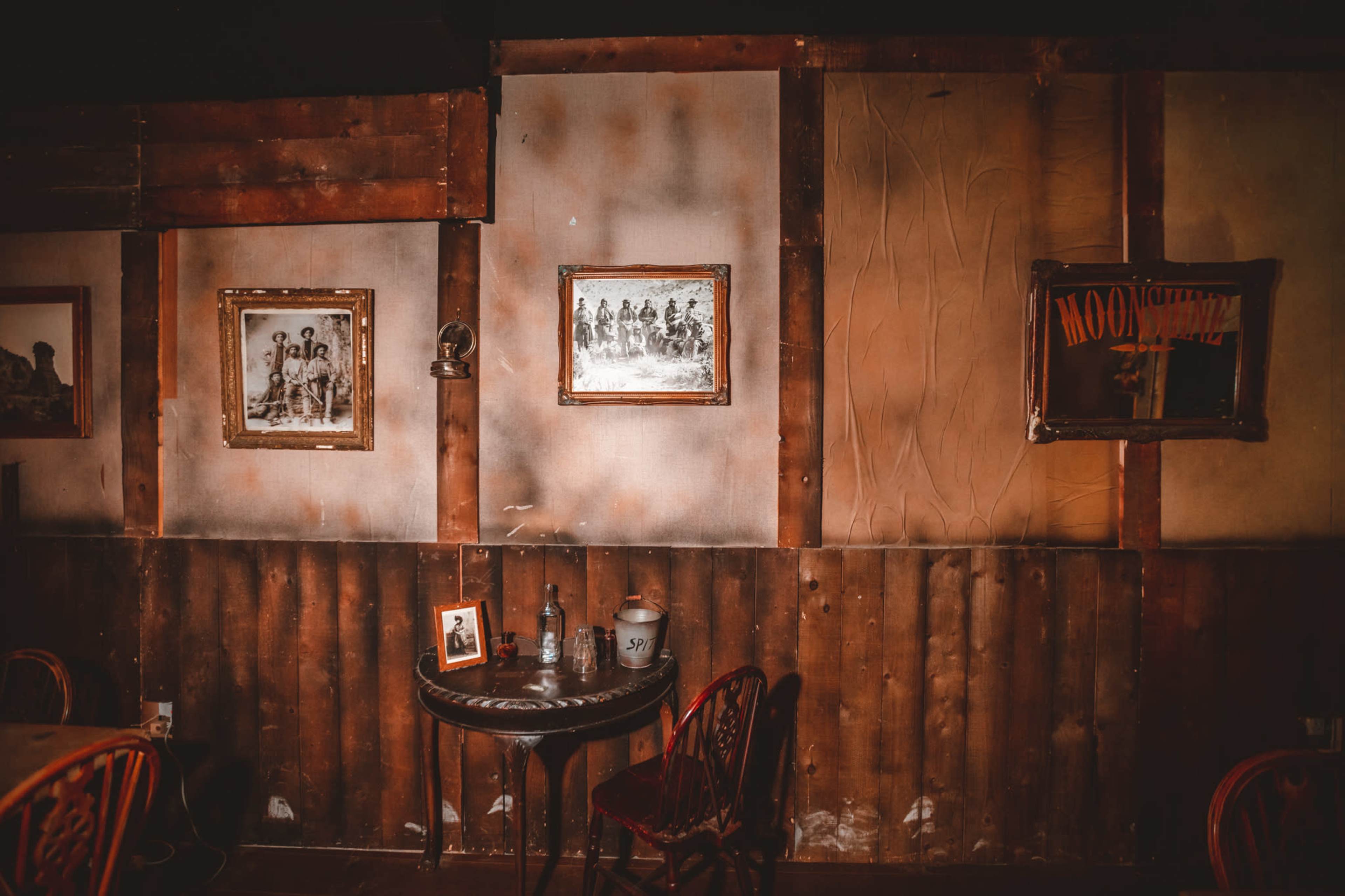 A rustic interior of a room with wooden walls, framed pictures, and a small table set with various objects.