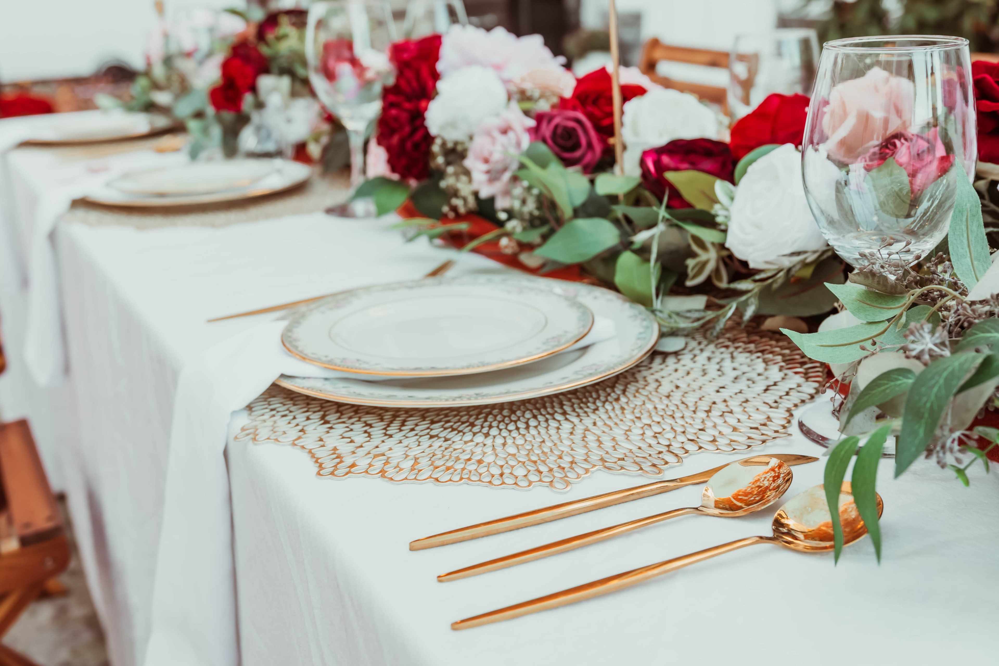 The image shows an elegantly set dining table adorned with floral arrangements and golden cutlery.