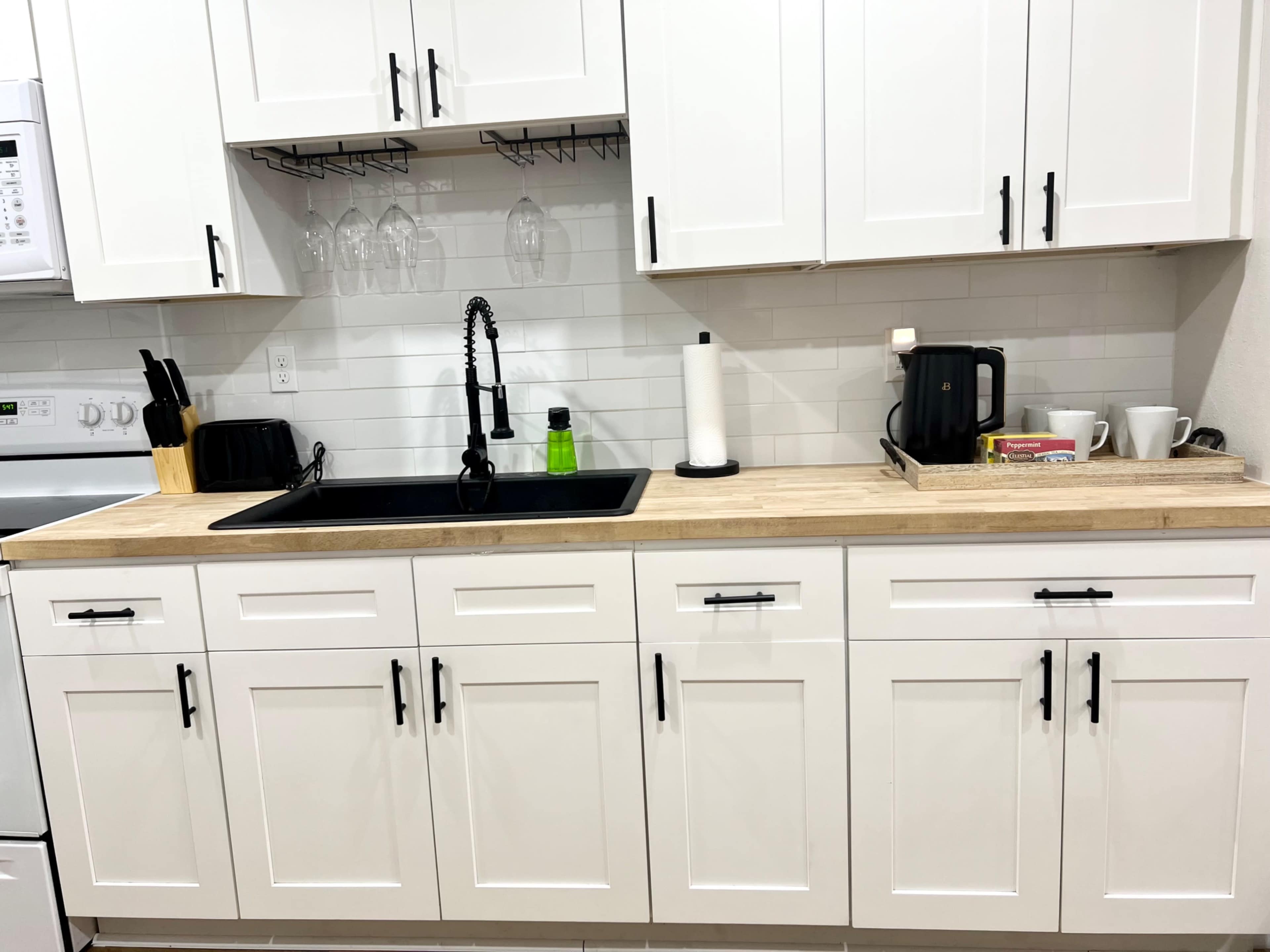 A modern kitchen with white cabinets, a black sink, and a wooden countertop featuring various kitchen appliances and utensils.
