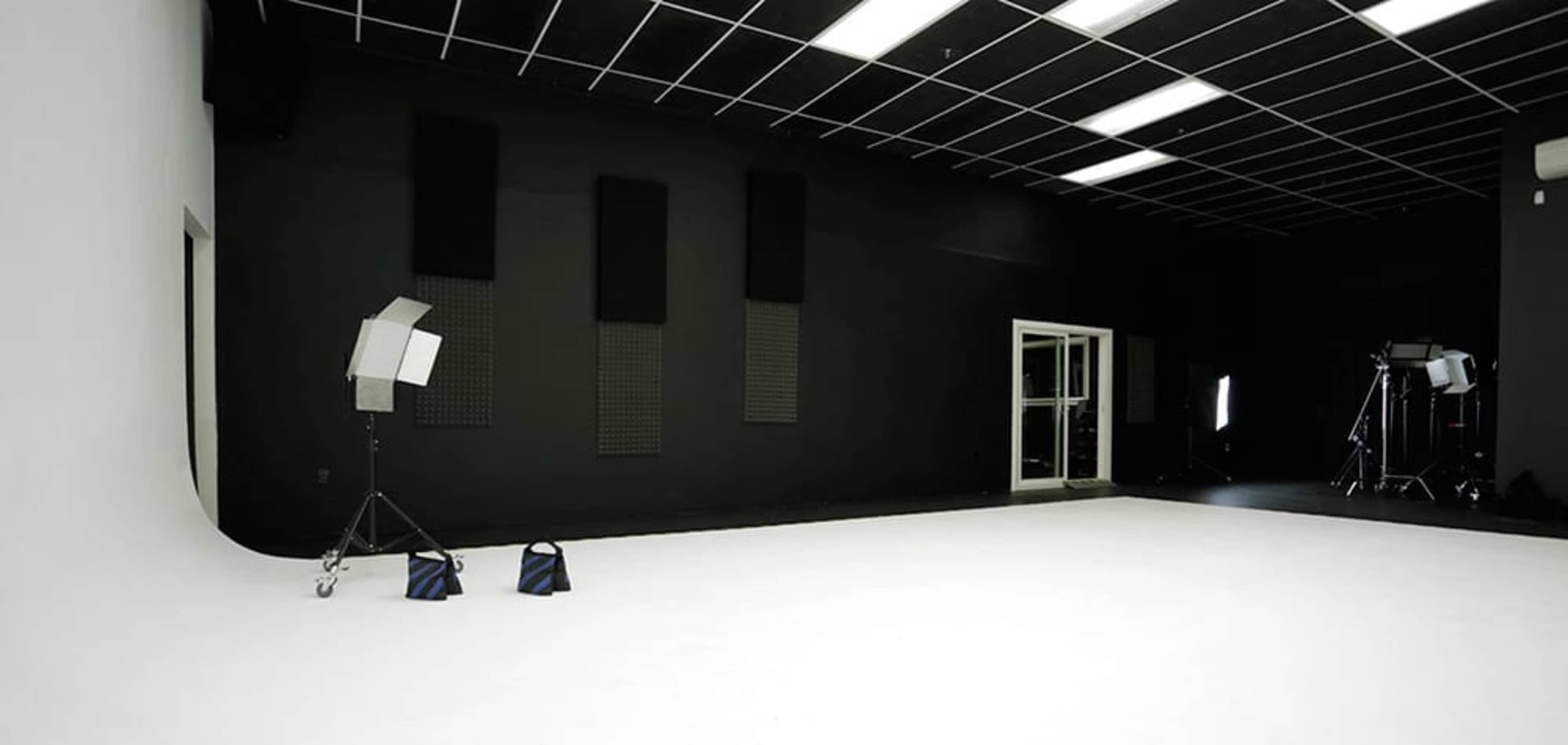 The image shows a spacious photo studio with a white backdrop, black walls, and various lighting equipment set up in the corner.