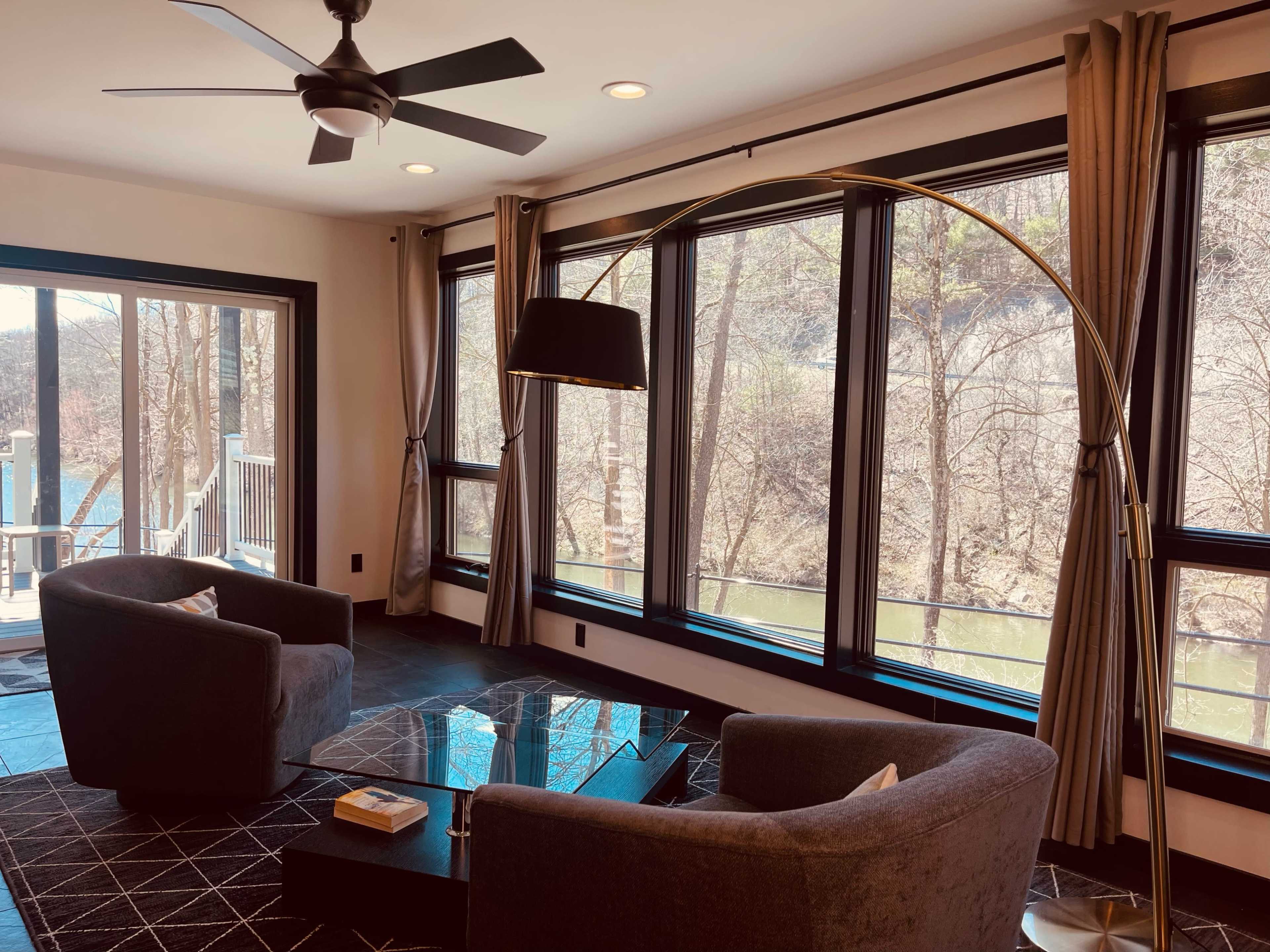 A modern living area with two gray armchairs, a floor lamp, and large windows overlooking a natural view.
