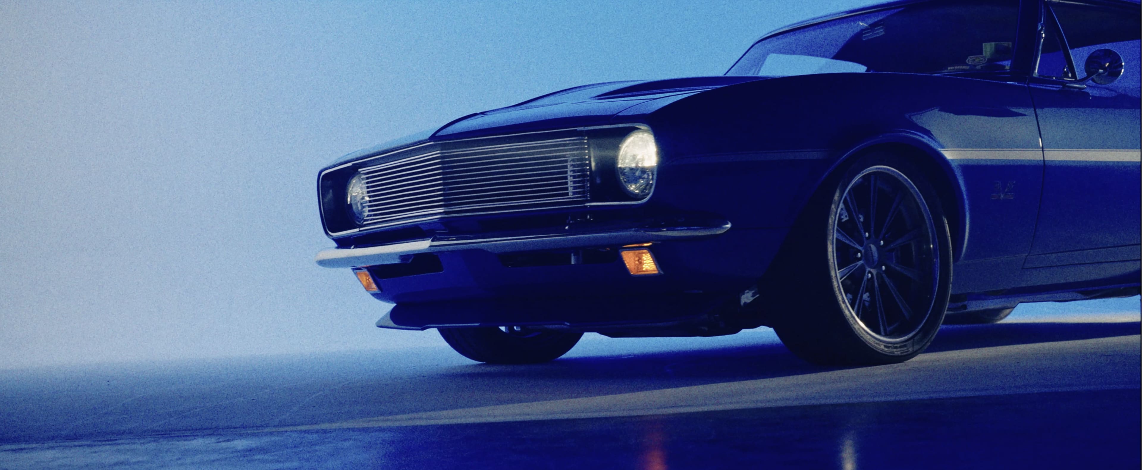 A vintage black muscle car is parked in a studio with a blue backdrop, showcasing its chrome grille and sleek design.