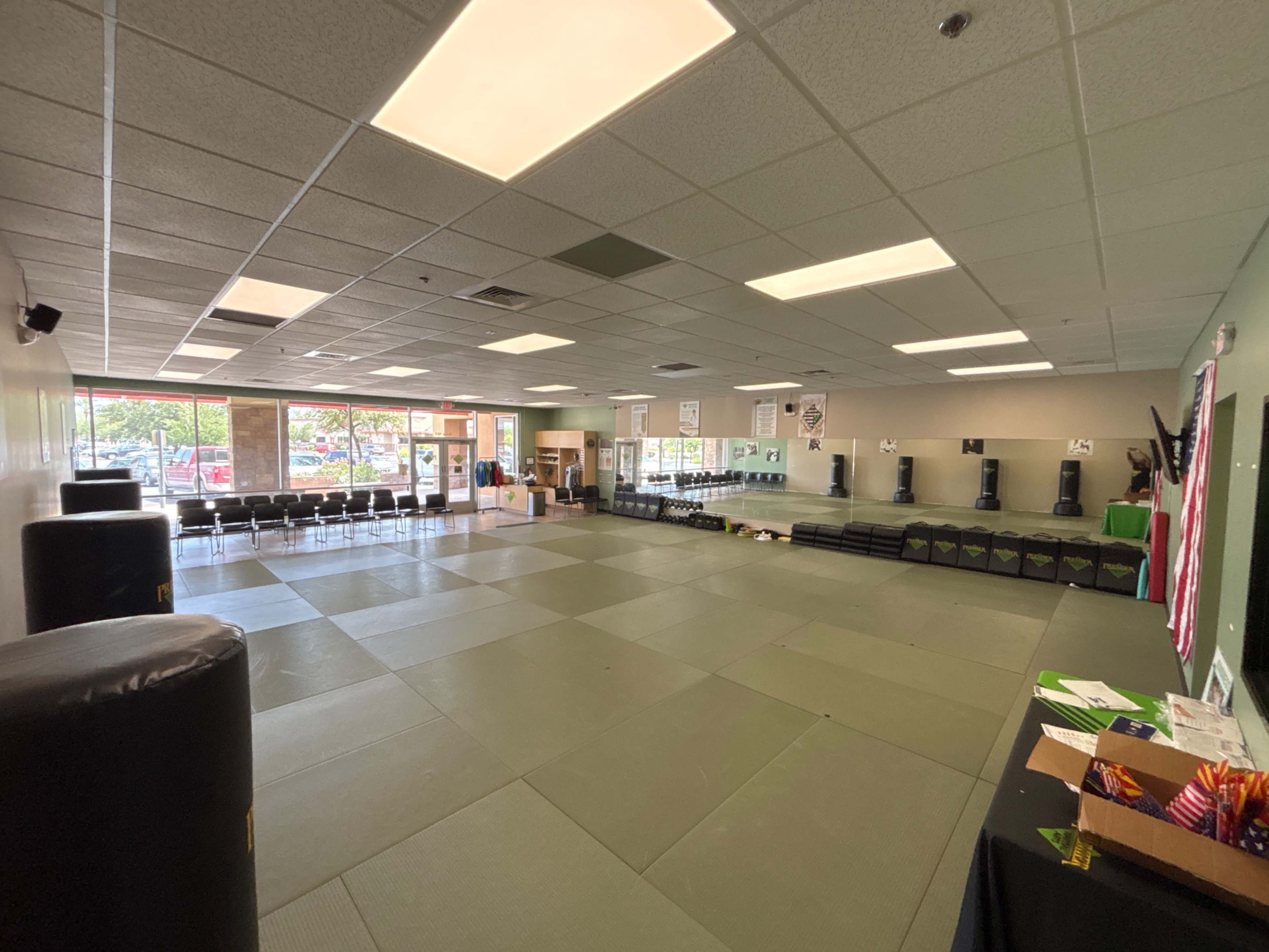 The image shows an empty martial arts dojo with padded flooring and a row of black training equipment along the walls.