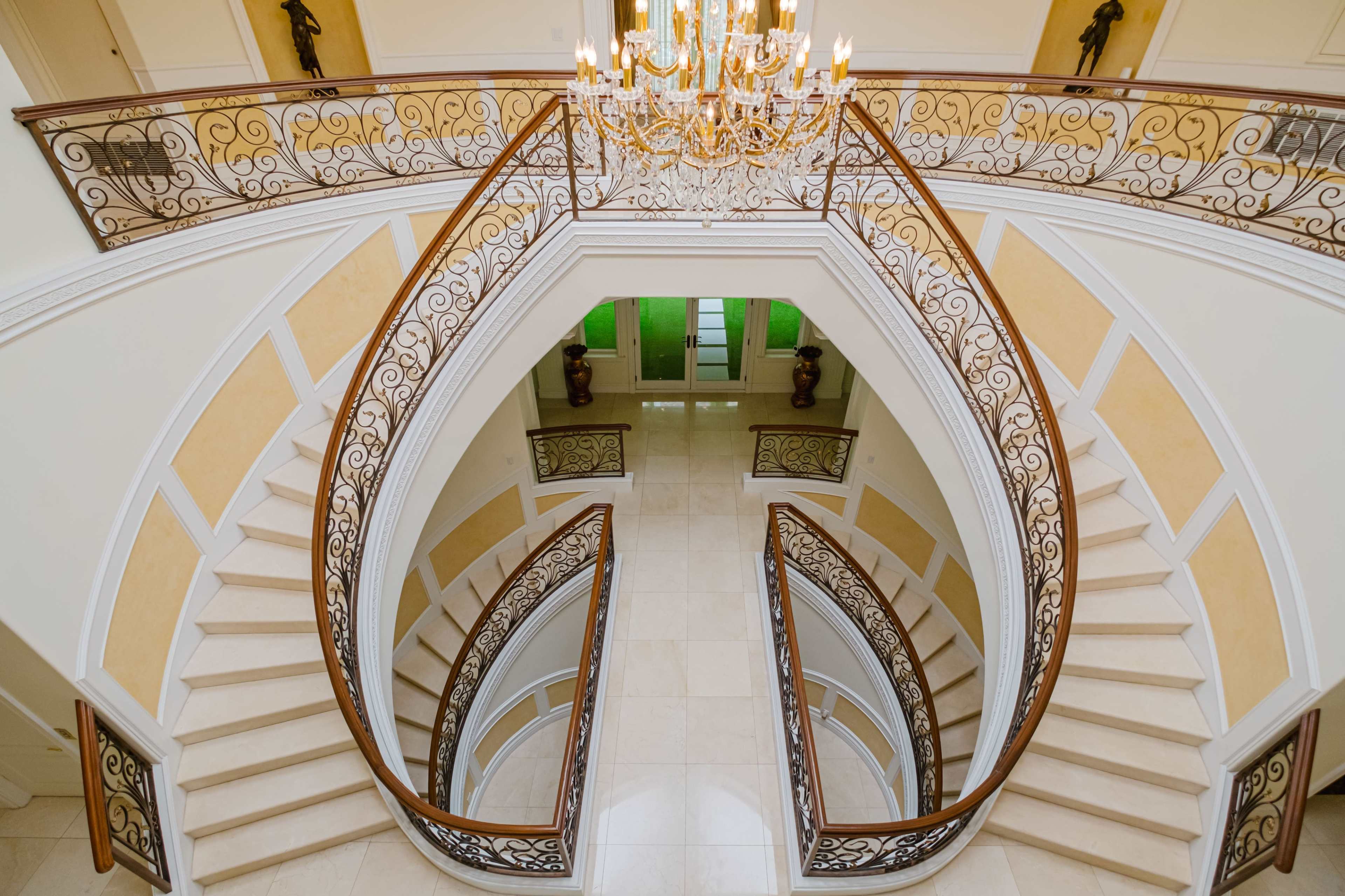 An elegant staircase with curved wooden railings and a chandelier above, set in a spacious foyer.