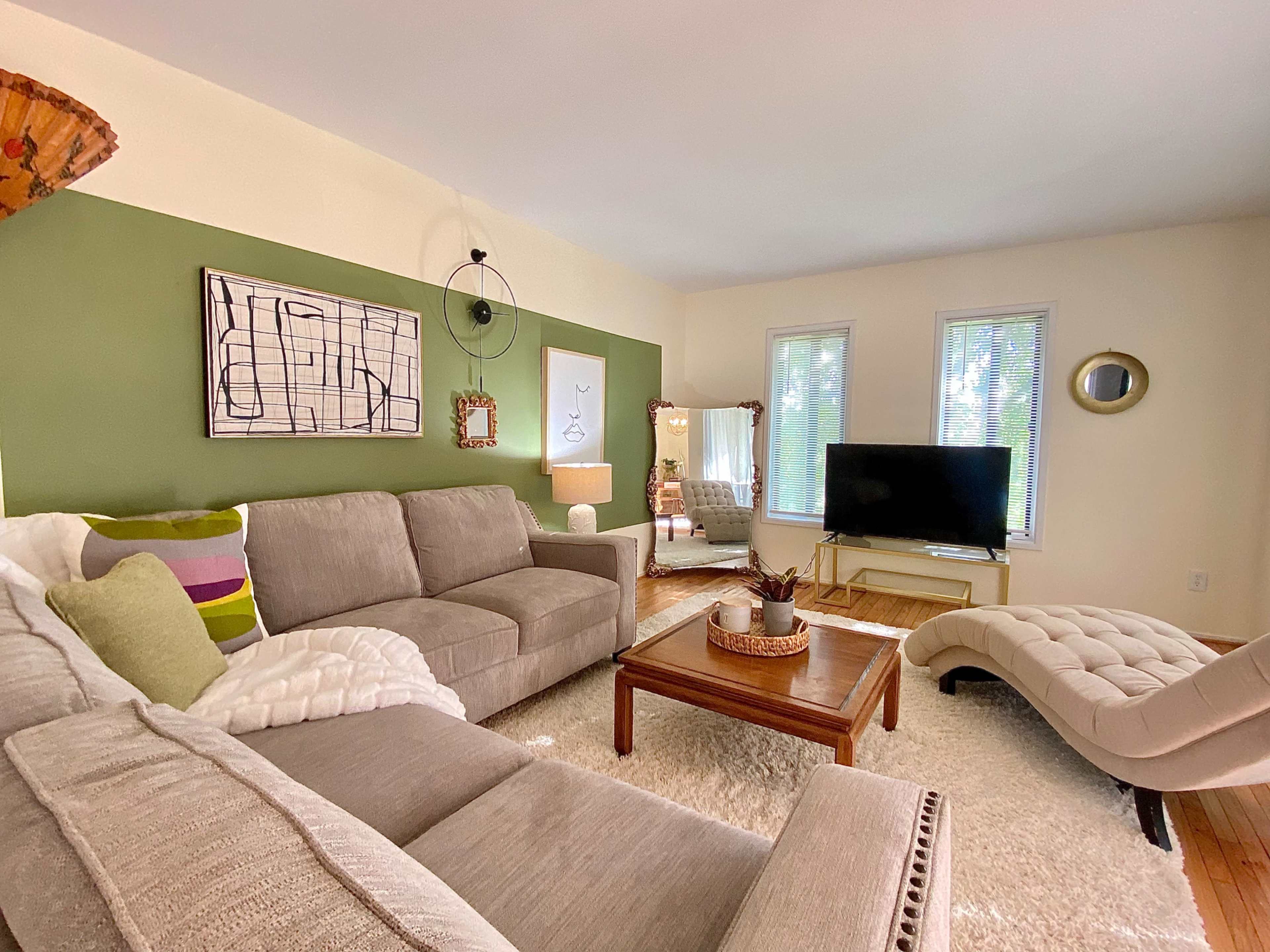 A living room with a sectional sofa, a coffee table, a television on a stand, and large windows letting in natural light.