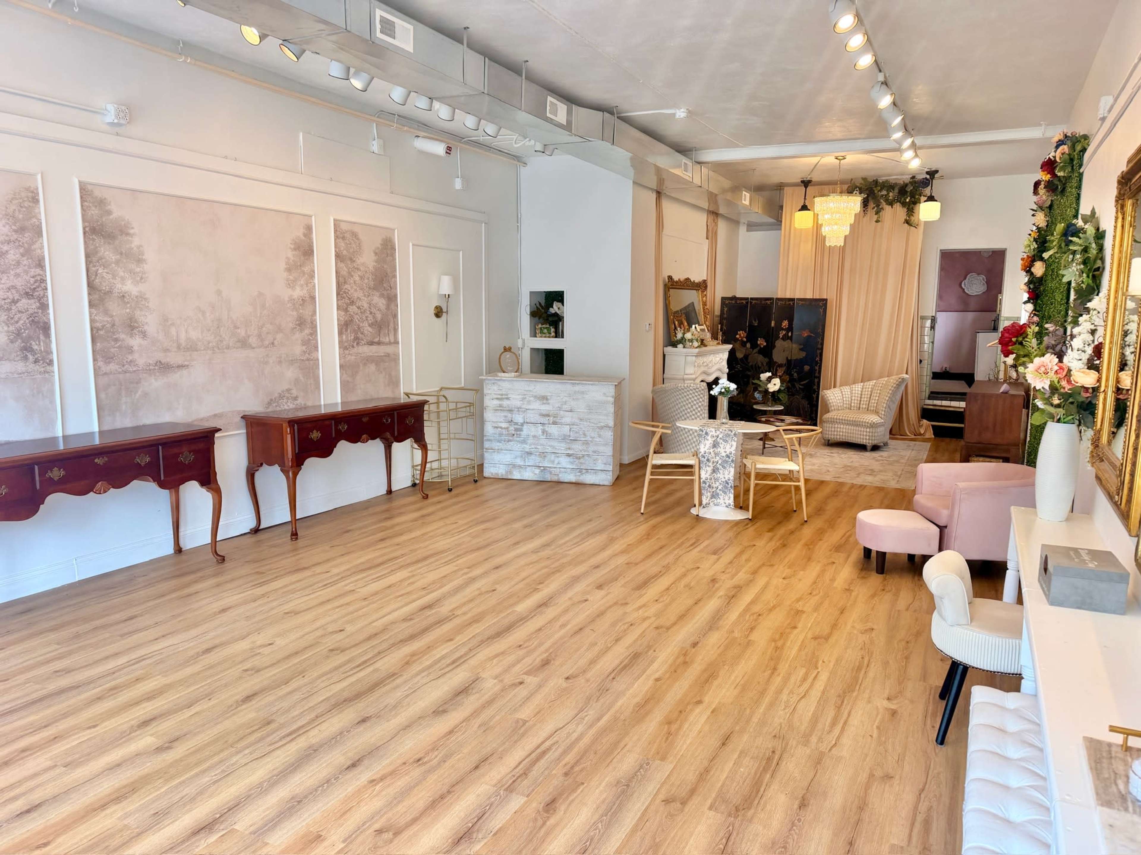 The image shows a spacious, well-lit interior of a boutique or event space featuring light wood flooring, elegant furniture, and decorative elements along the walls.