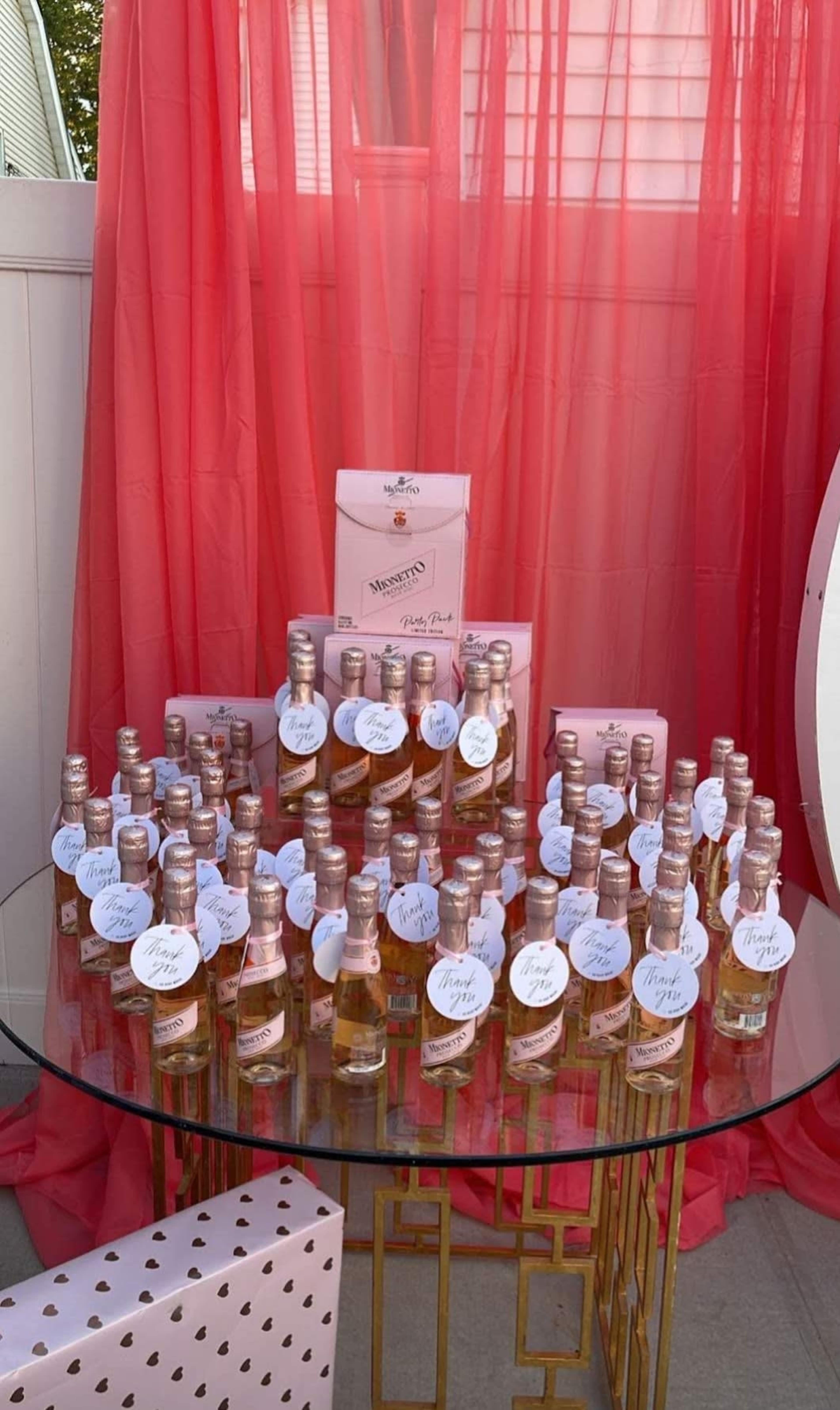A glass table displays numerous small bottles of rosé wine, arranged neatly beneath a coral-colored backdrop.