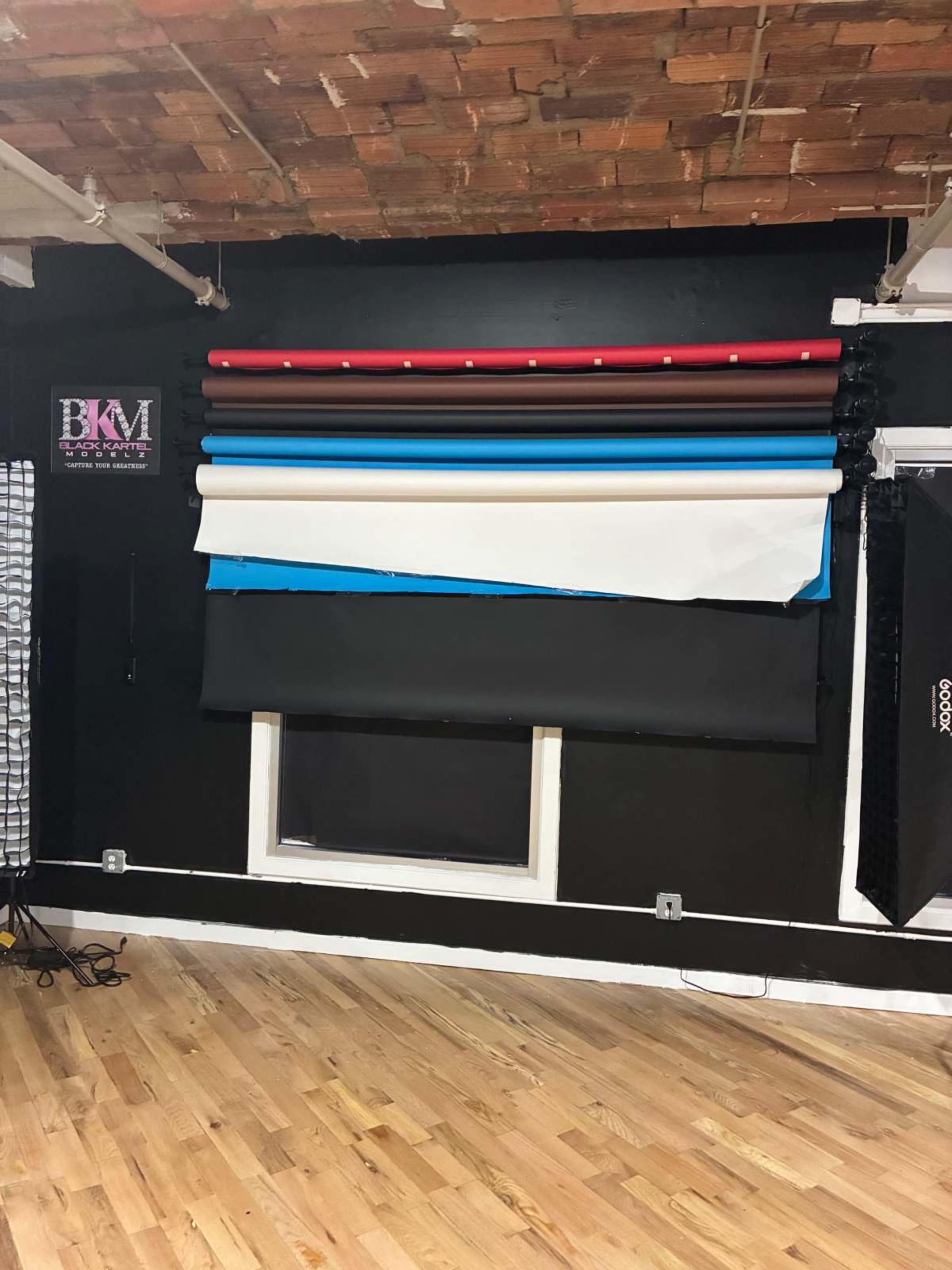 The image shows a wall with various colored backdrop rolls mounted above a window in a studio setting.