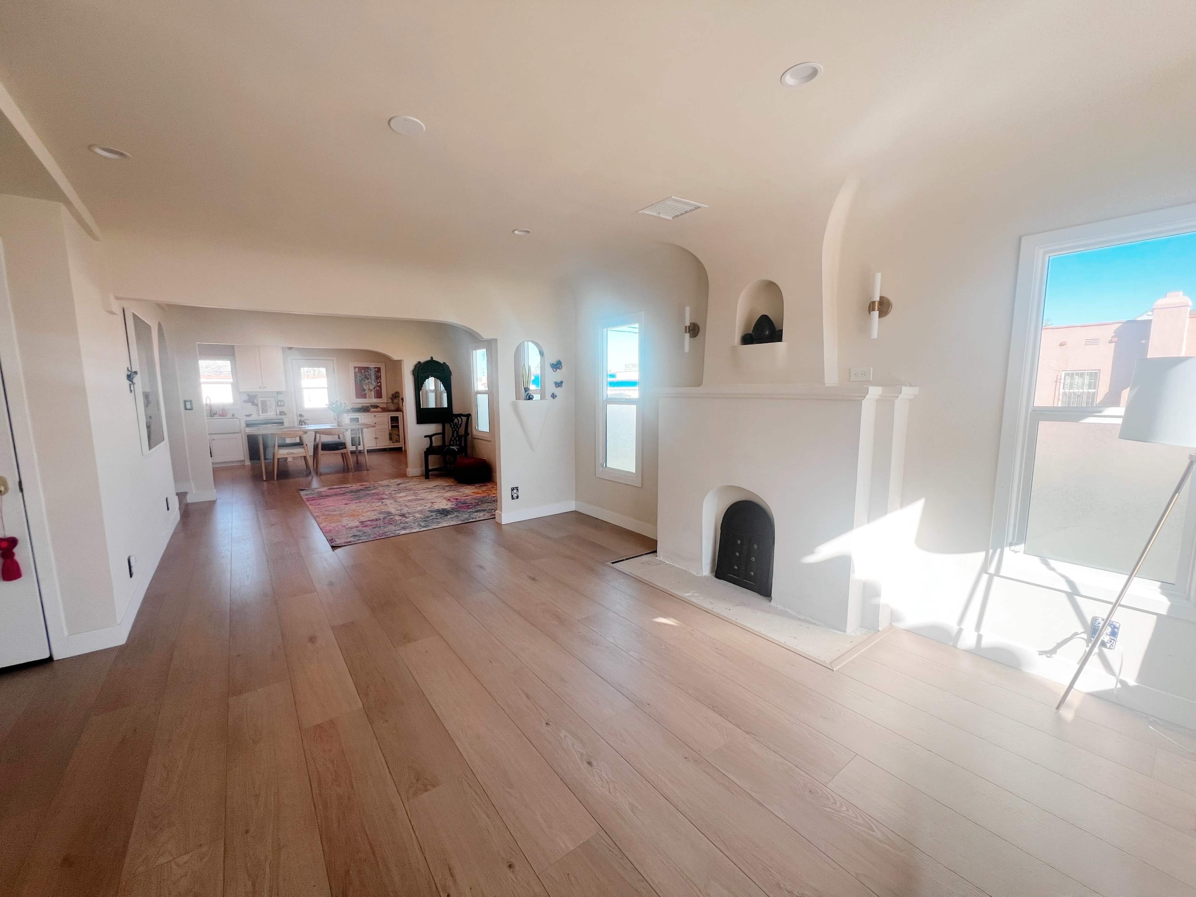 The image shows a spacious, light-filled living area featuring a fireplace, wooden flooring, and a view of an adjacent dining space.