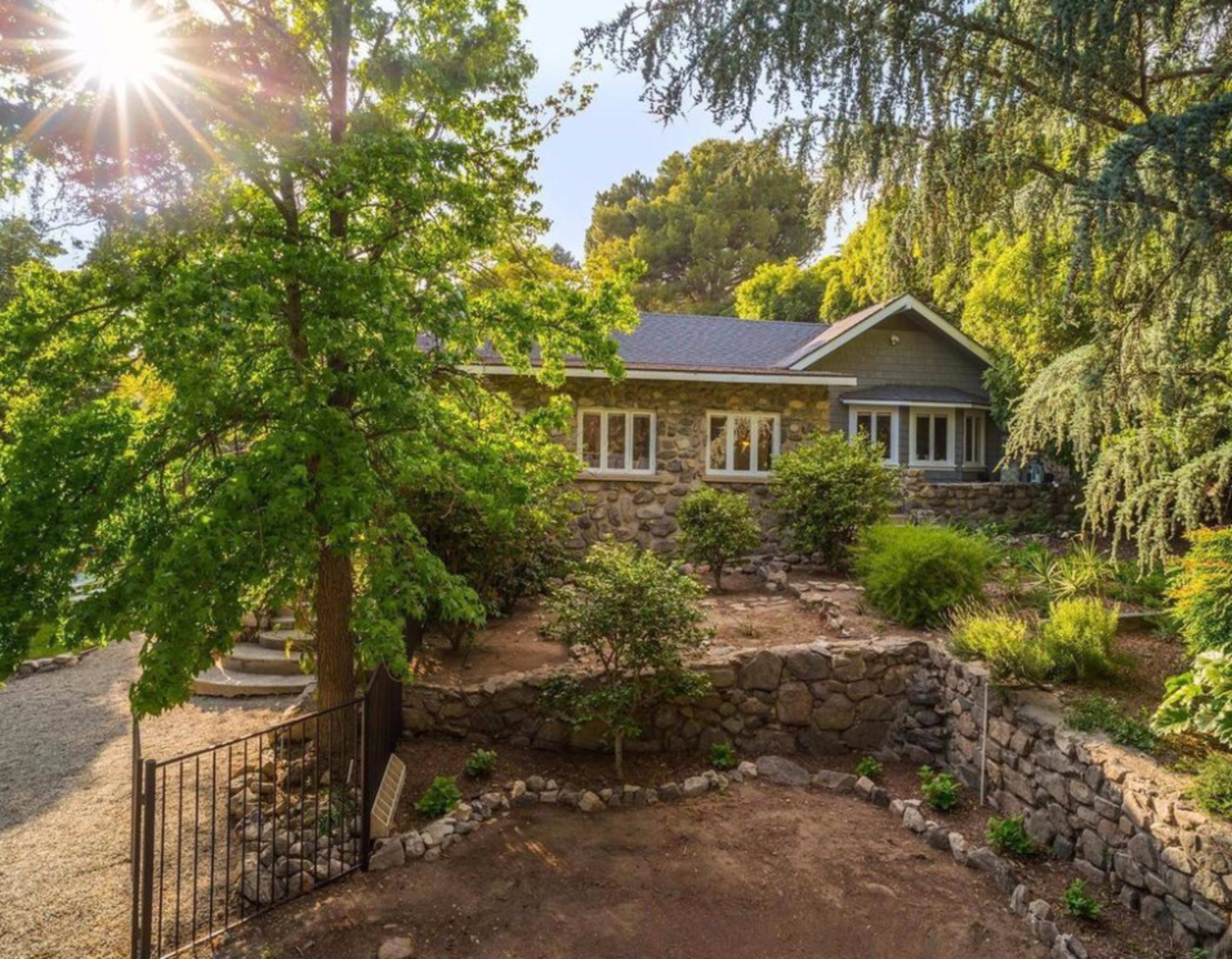A stone-faced house is nestled among lush greenery and trees in a well-maintained garden setting.