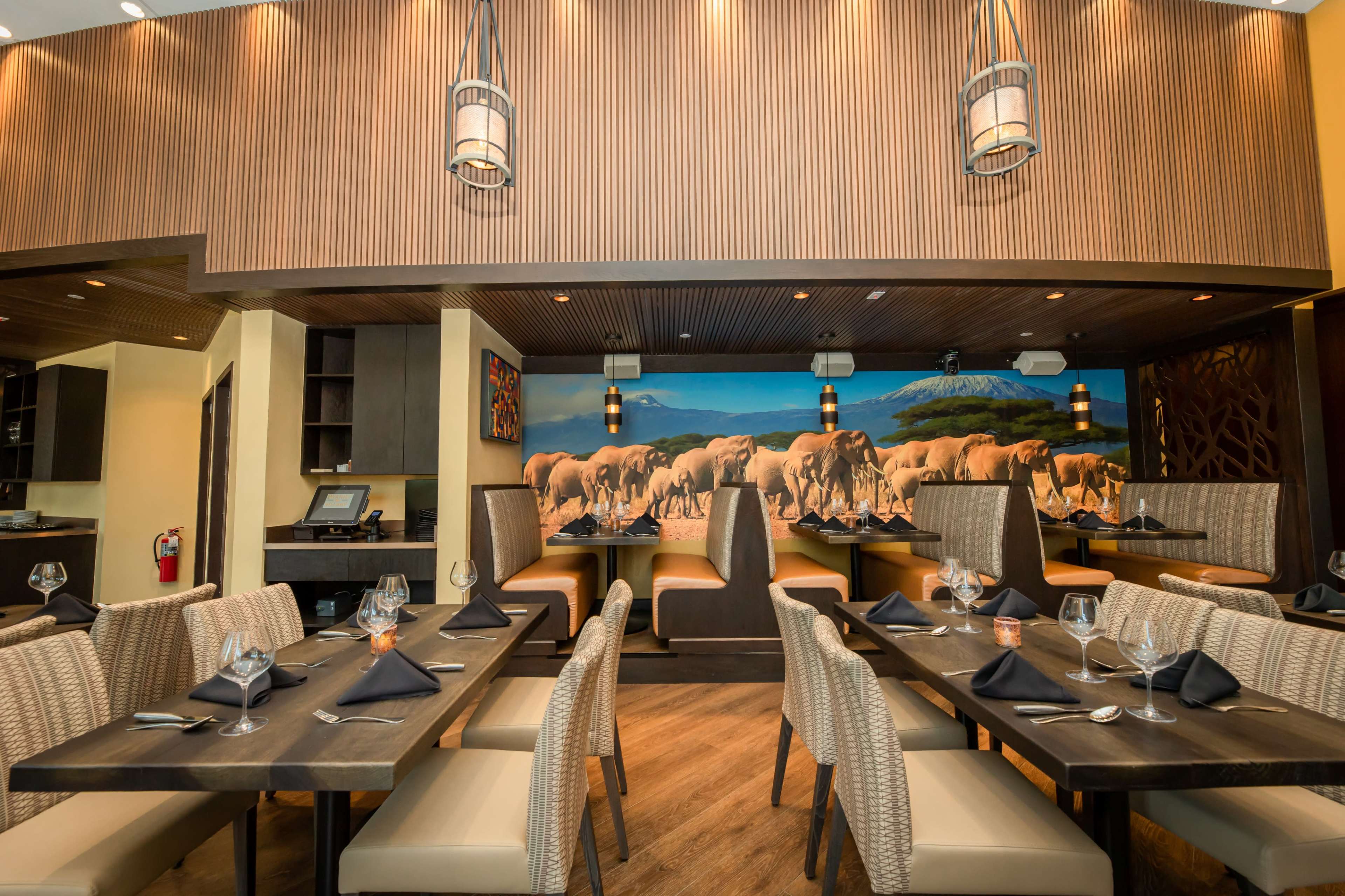A restaurant interior with wooden accents, tables set for dining, and a wall mural depicting elephants in a natural setting.