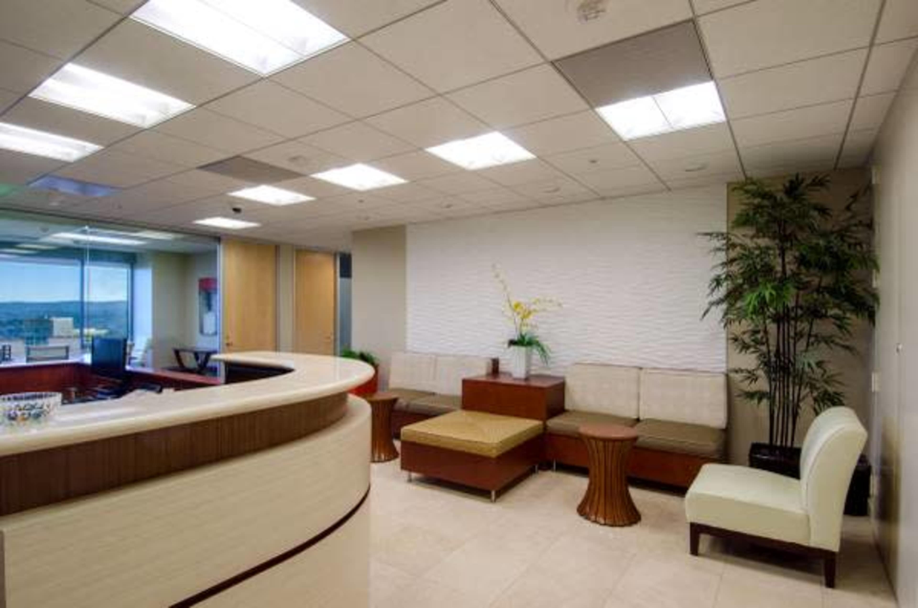 A modern office waiting area with beige seating, wooden tables, and a decorative plant against a textured wall.